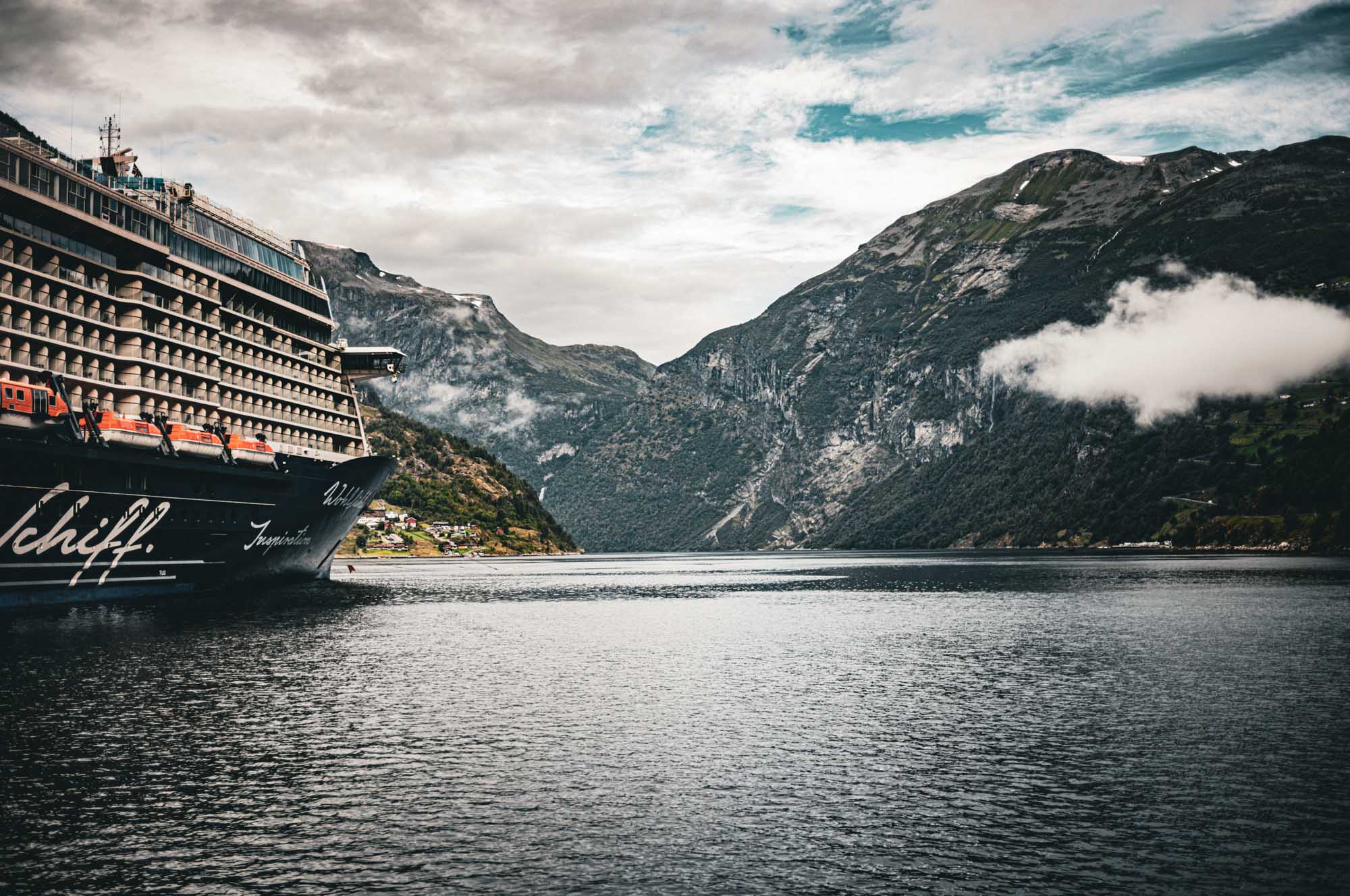 Cruise ship in scenic fjord with misty mountains under a cloudy sky.
