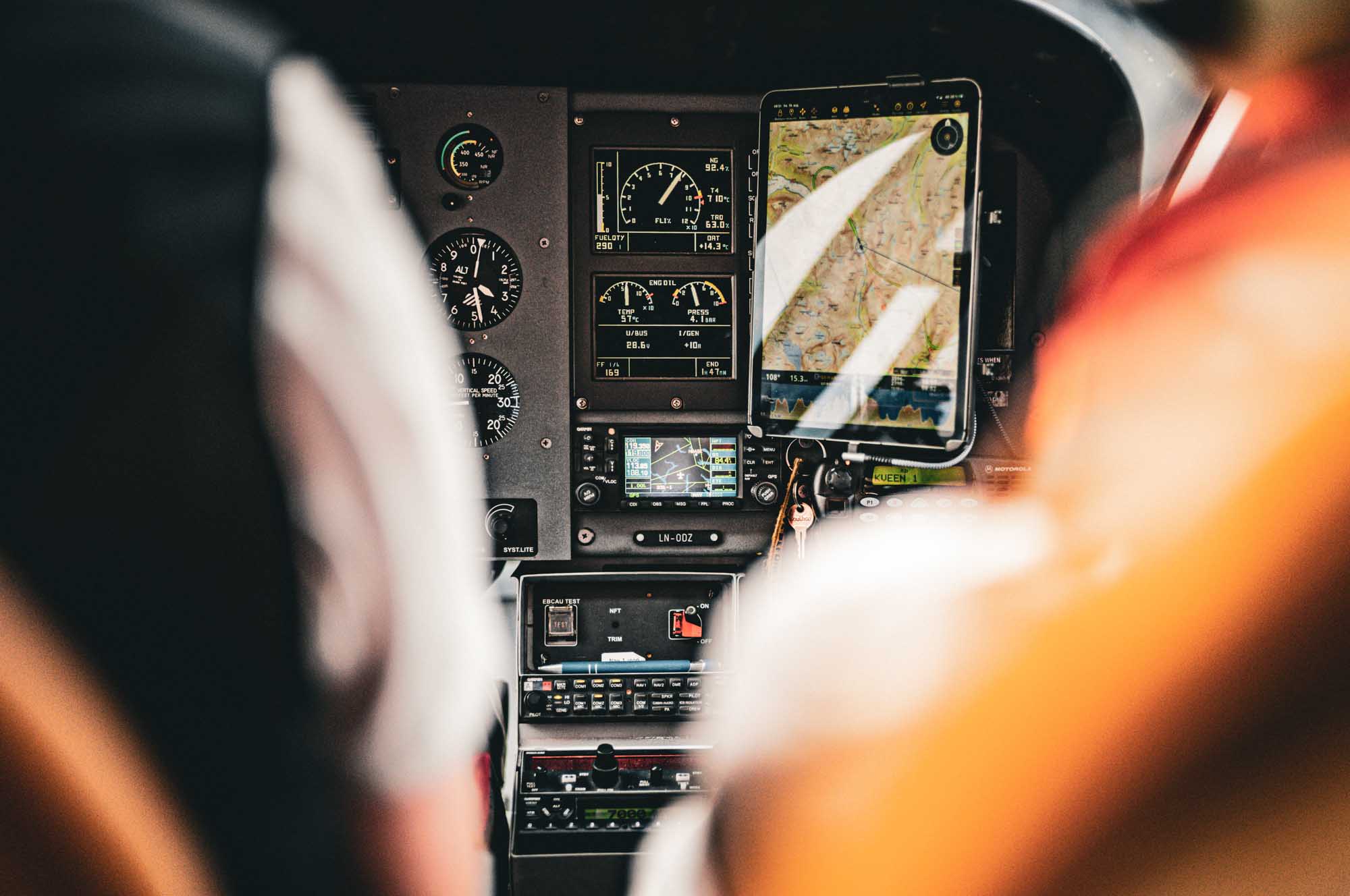 Cockpit dashboard with aviation instruments and GPS map display, viewed between pilot seats with blurred foreground.