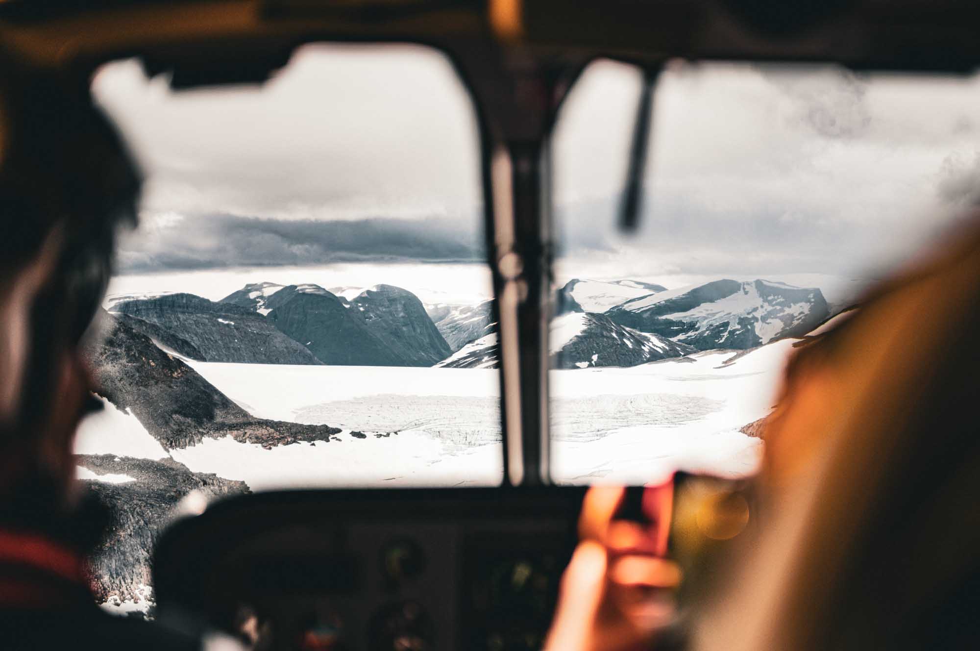 Aerial view of snowy mountains and glaciers through cockpit window on a cloudy day.