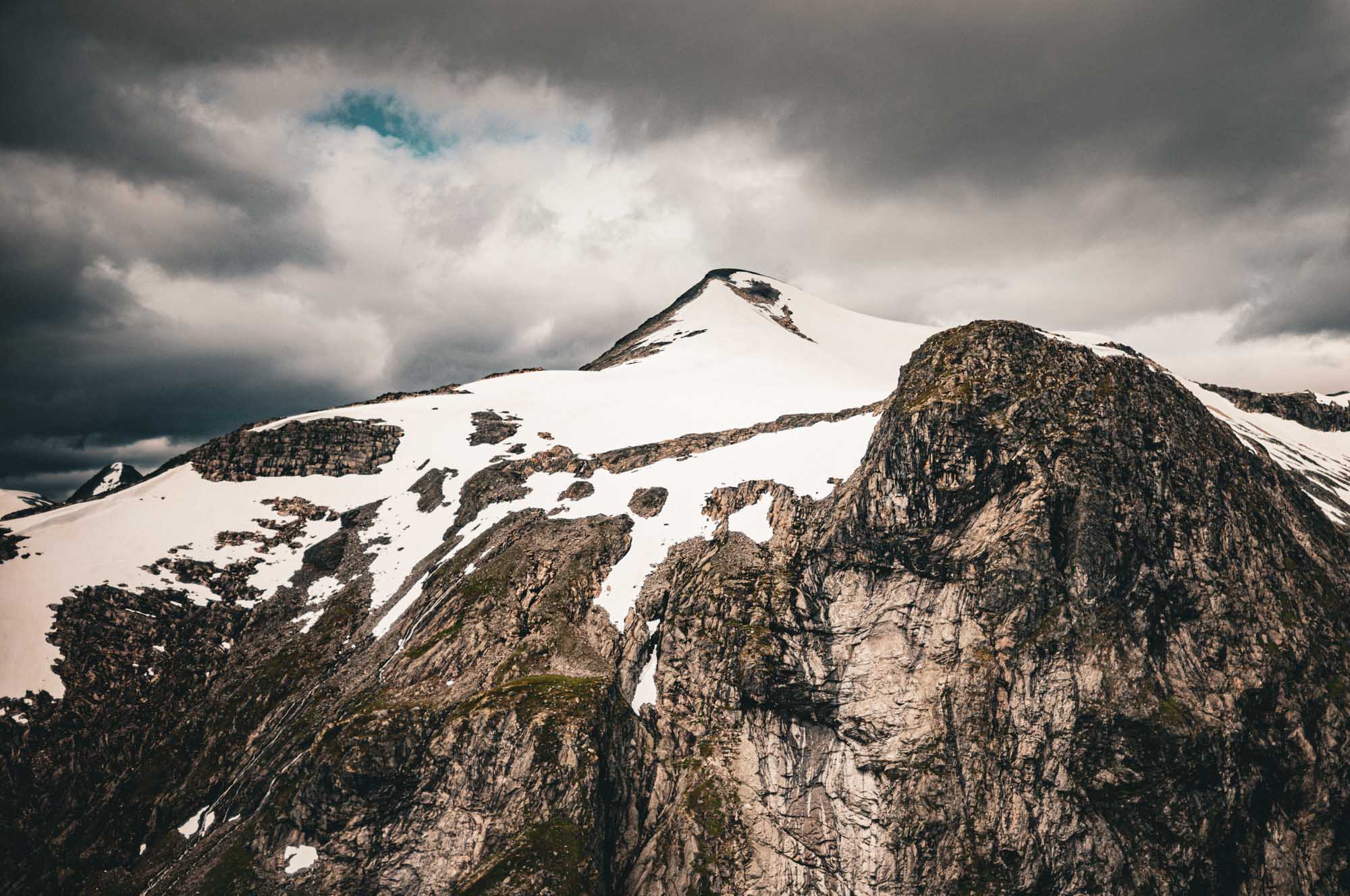 Snow-capped mountain peak under cloudy sky, showcasing rugged rock formations and dramatic landscape.