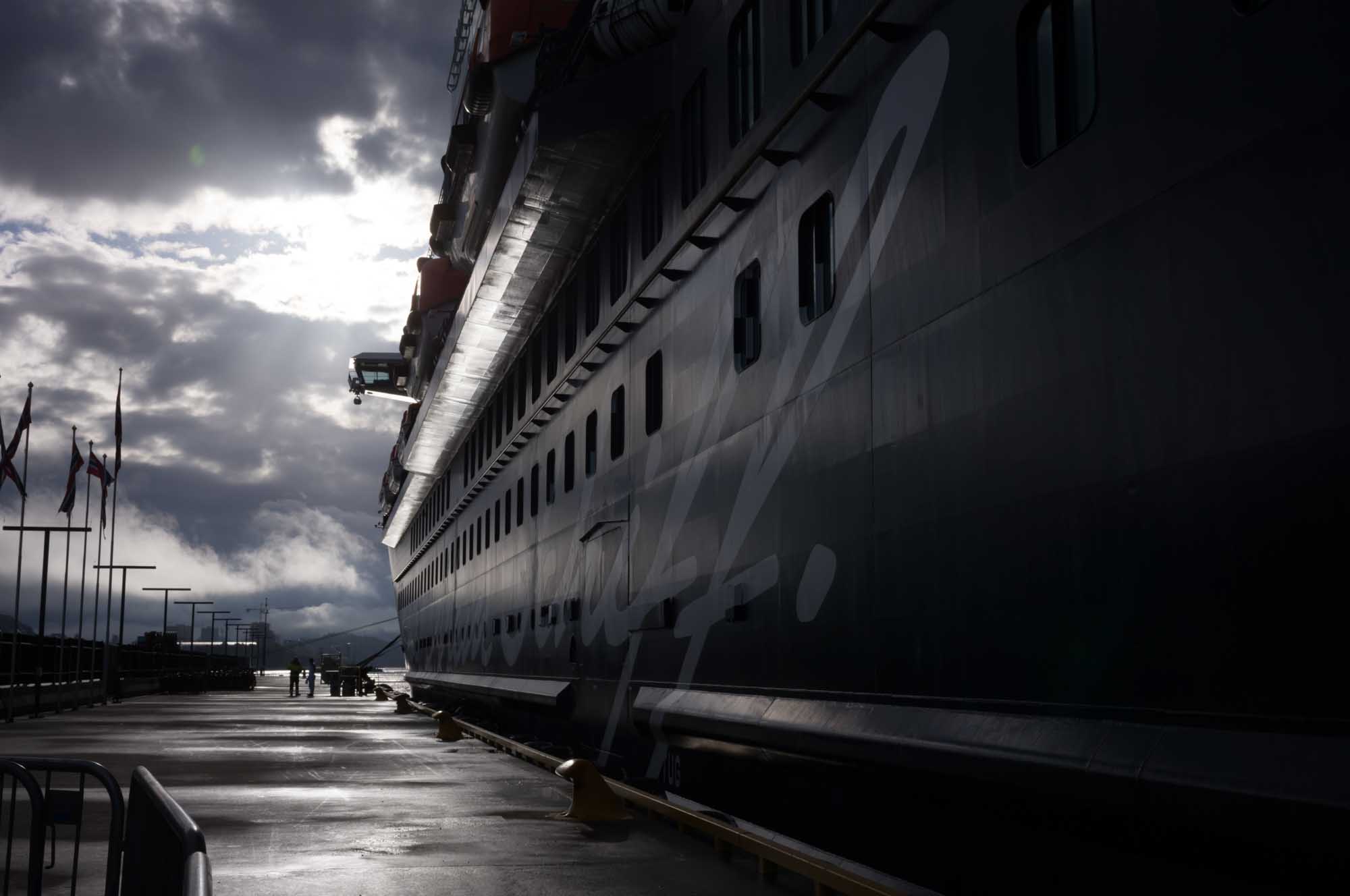 Cruise ship docked under cloudy sky with people walking along the pier.