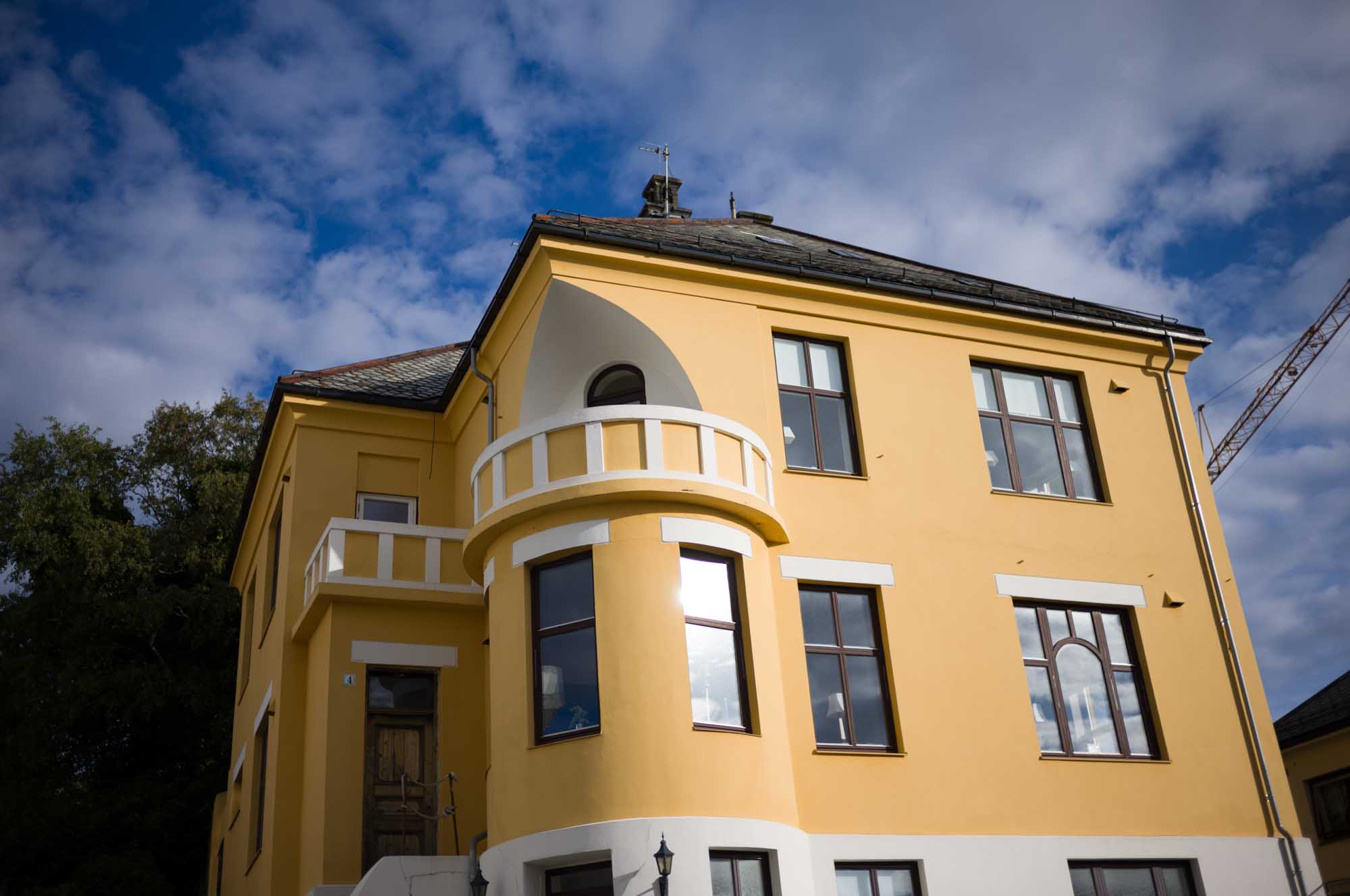 Yellow building with arched balcony and windows, set against a blue sky with clouds.