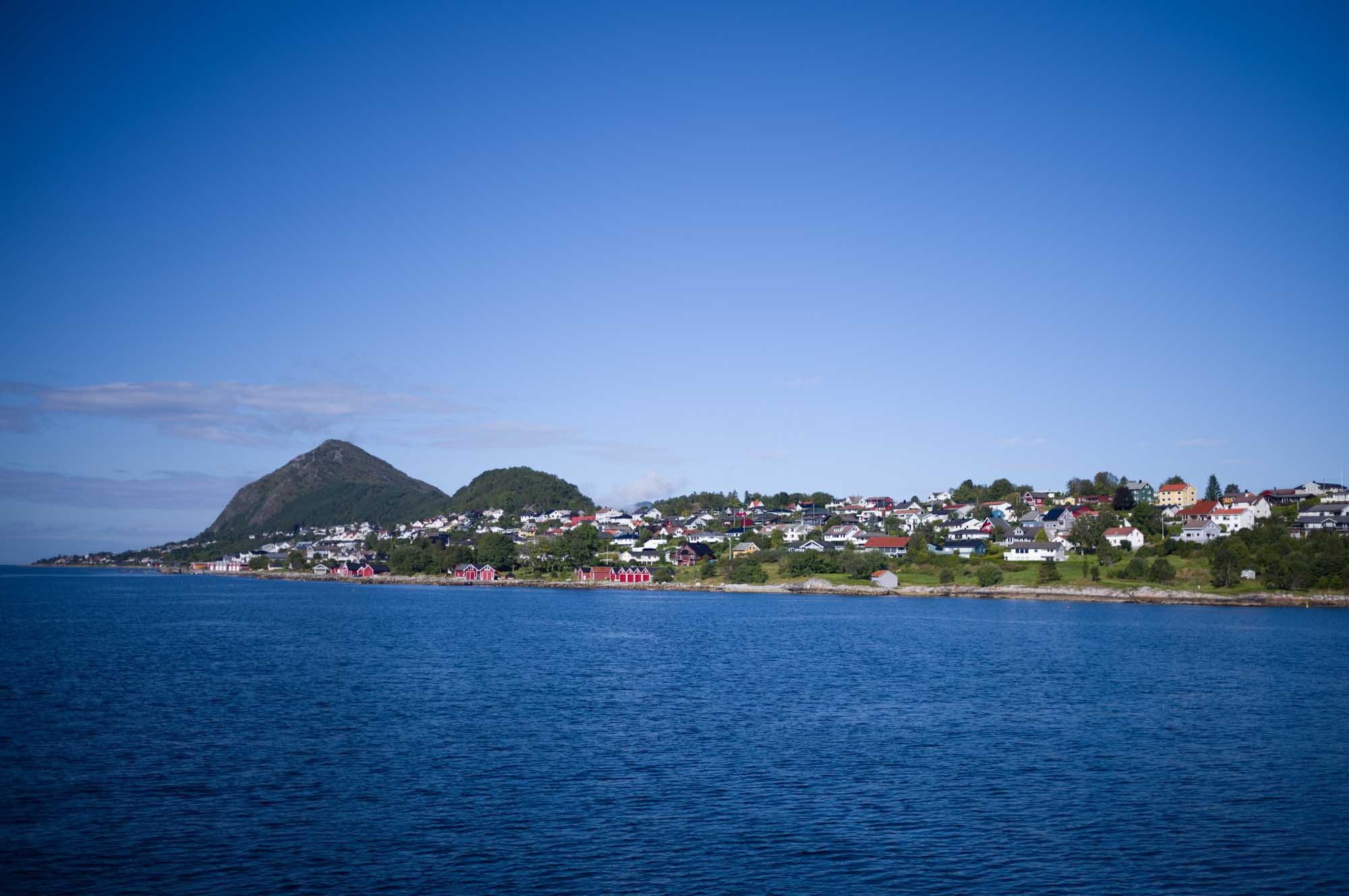 Coastal town with colorful houses, mountains, and a clear blue sky by a calm ocean.