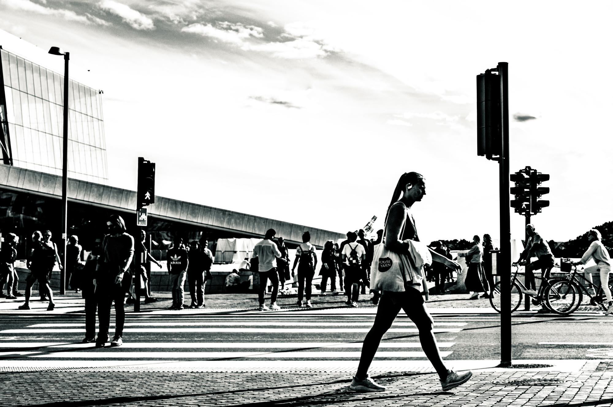 Silhouetted pedestrians crossing a busy street with modern architecture and traffic lights in the background.