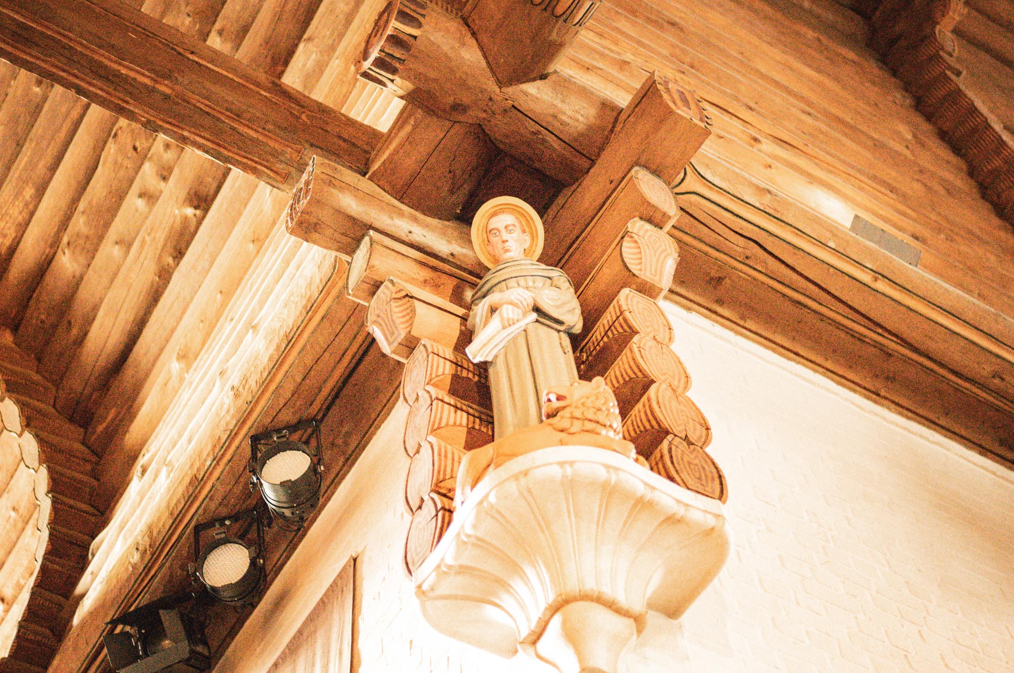 Wooden church ceiling with a religious statue and spotlight fixtures.
