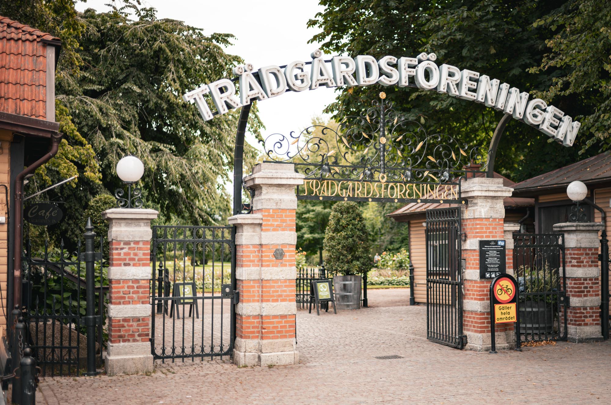 Entrance gate to Trädgårdsföreningen park with ornate ironwork and brick pillars, lush greenery in the background.