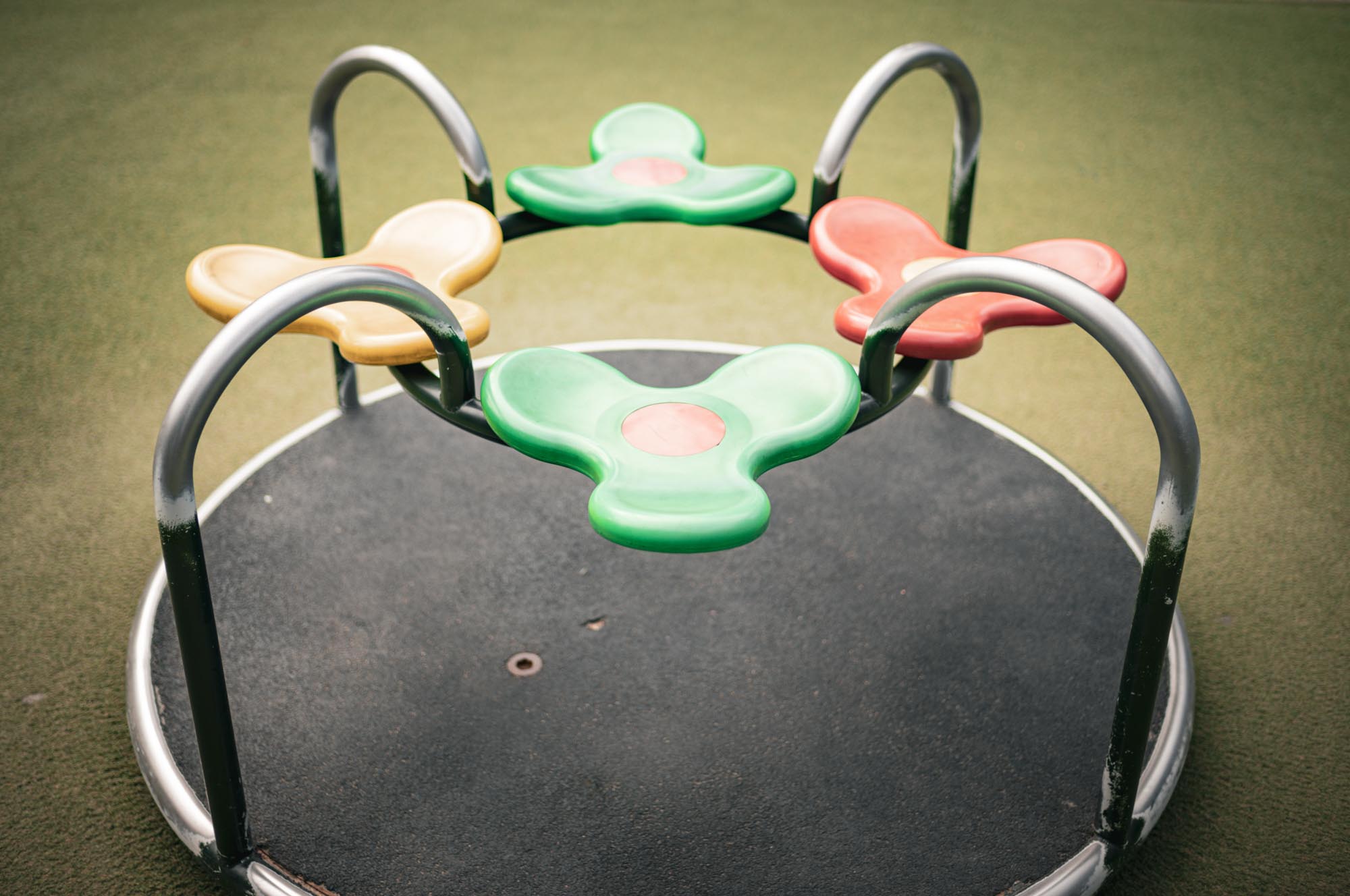 Colorful outdoor merry-go-round with three seats on a playground, featuring red, green, and yellow designs.
