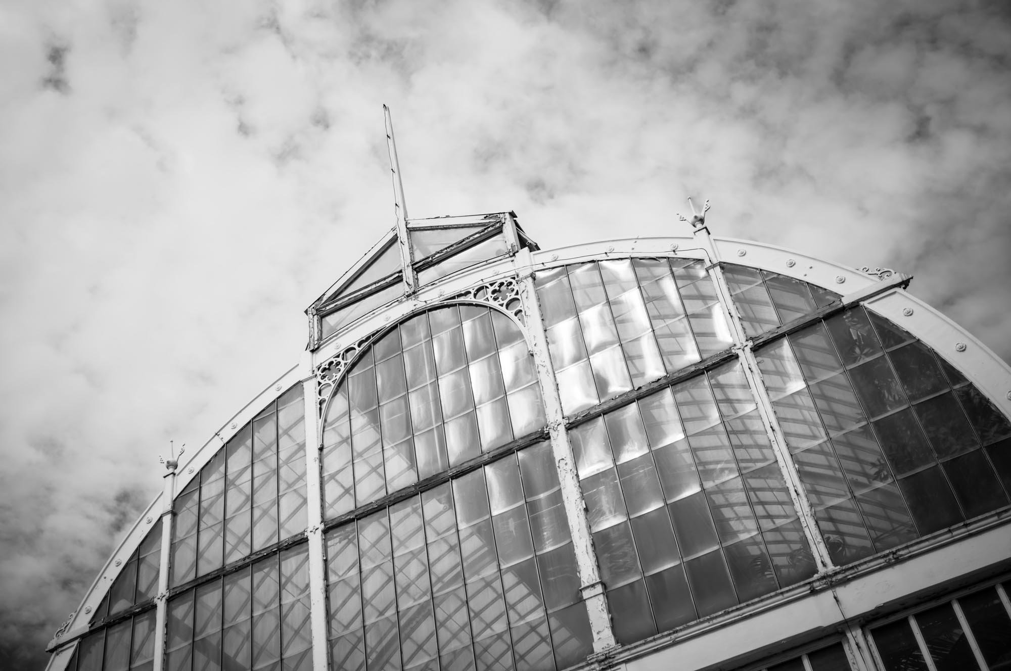 Black and white photo of a glass-domed greenhouse with cloudy sky backdrop.
