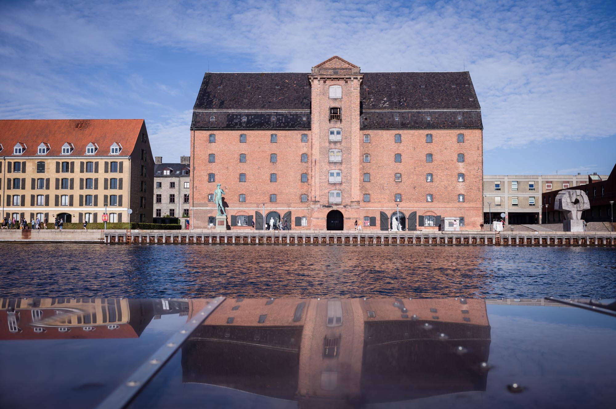 Historic brick building by a canal with clear sky reflection on water in Copenhagen, Denmark.