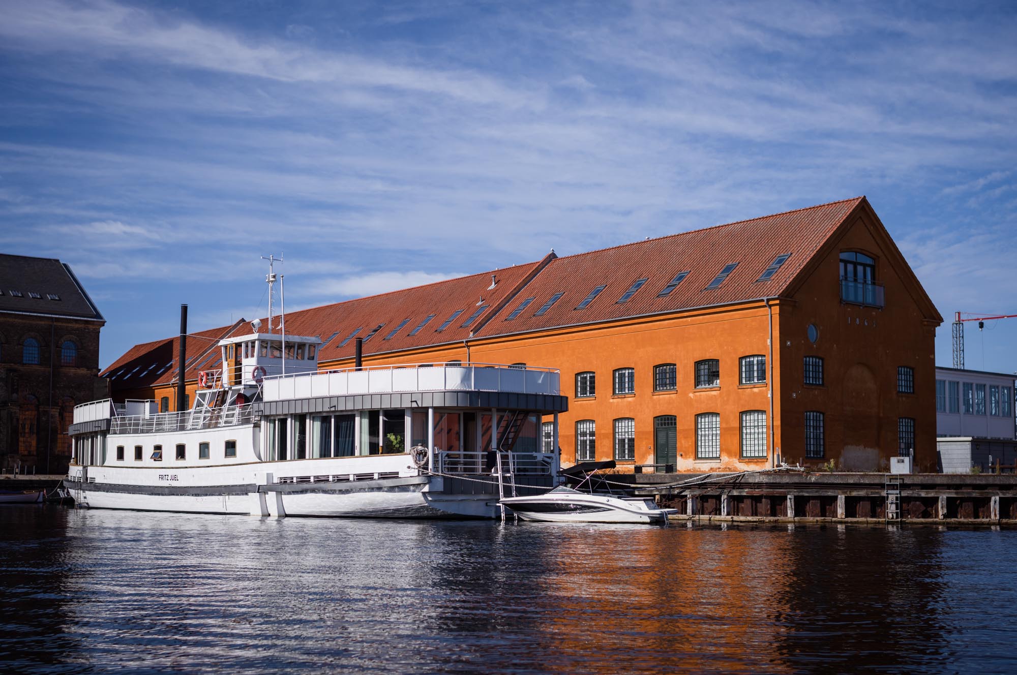 White boat docked by orange brick building under blue sky.