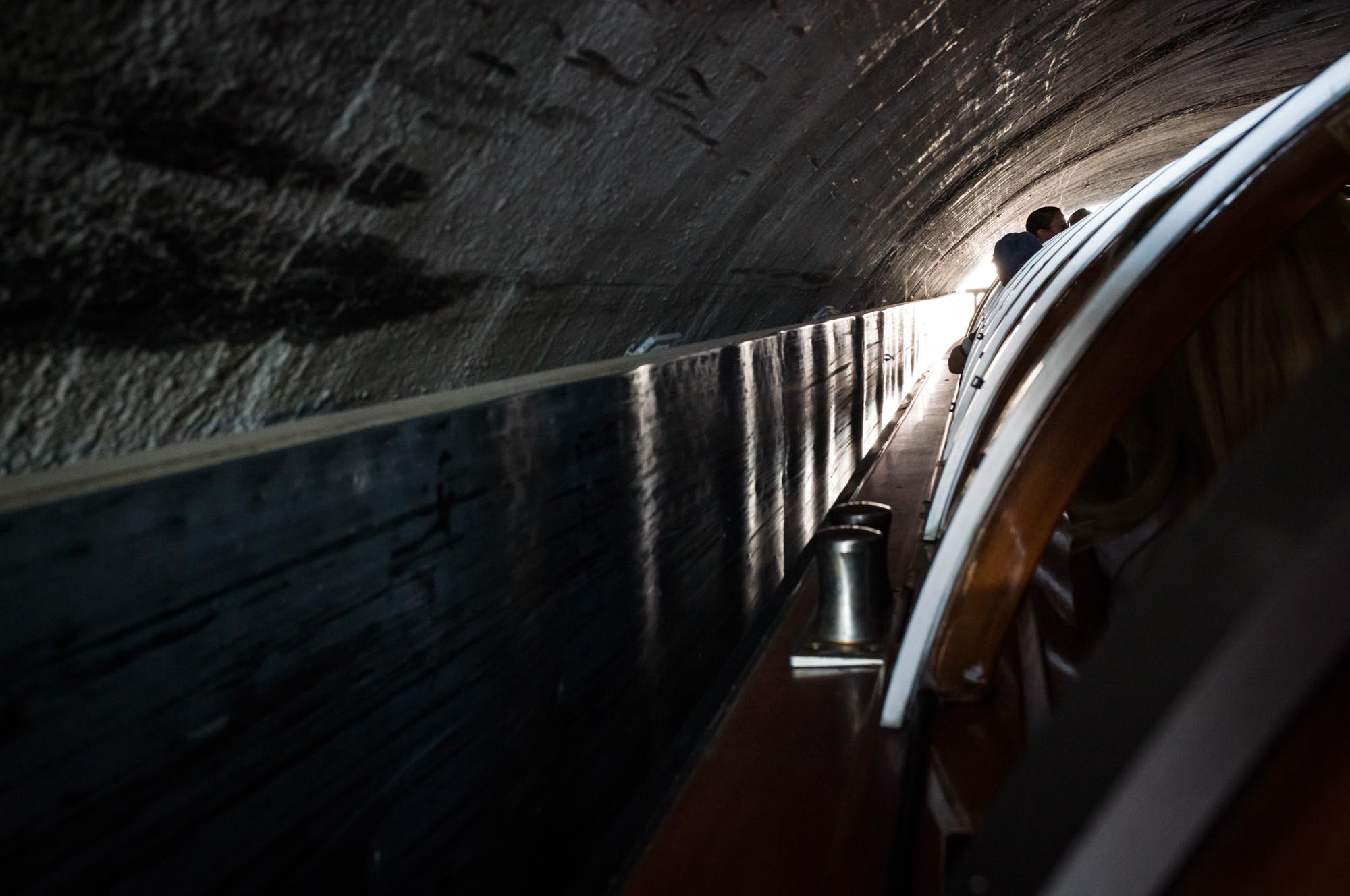 Boat navigating through a narrow, dimly-lit tunnel with light visible at the end.