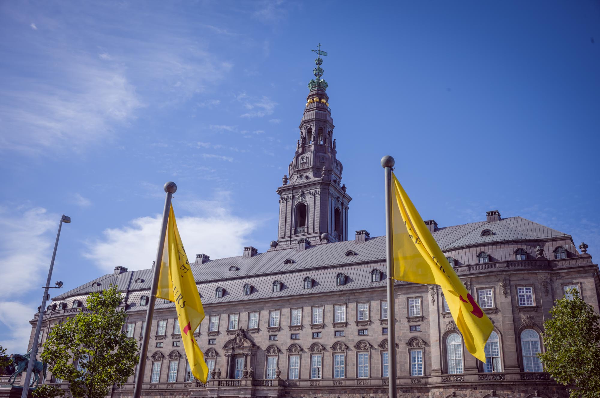 Historic building with a tall spire and yellow flags under a clear blue sky.