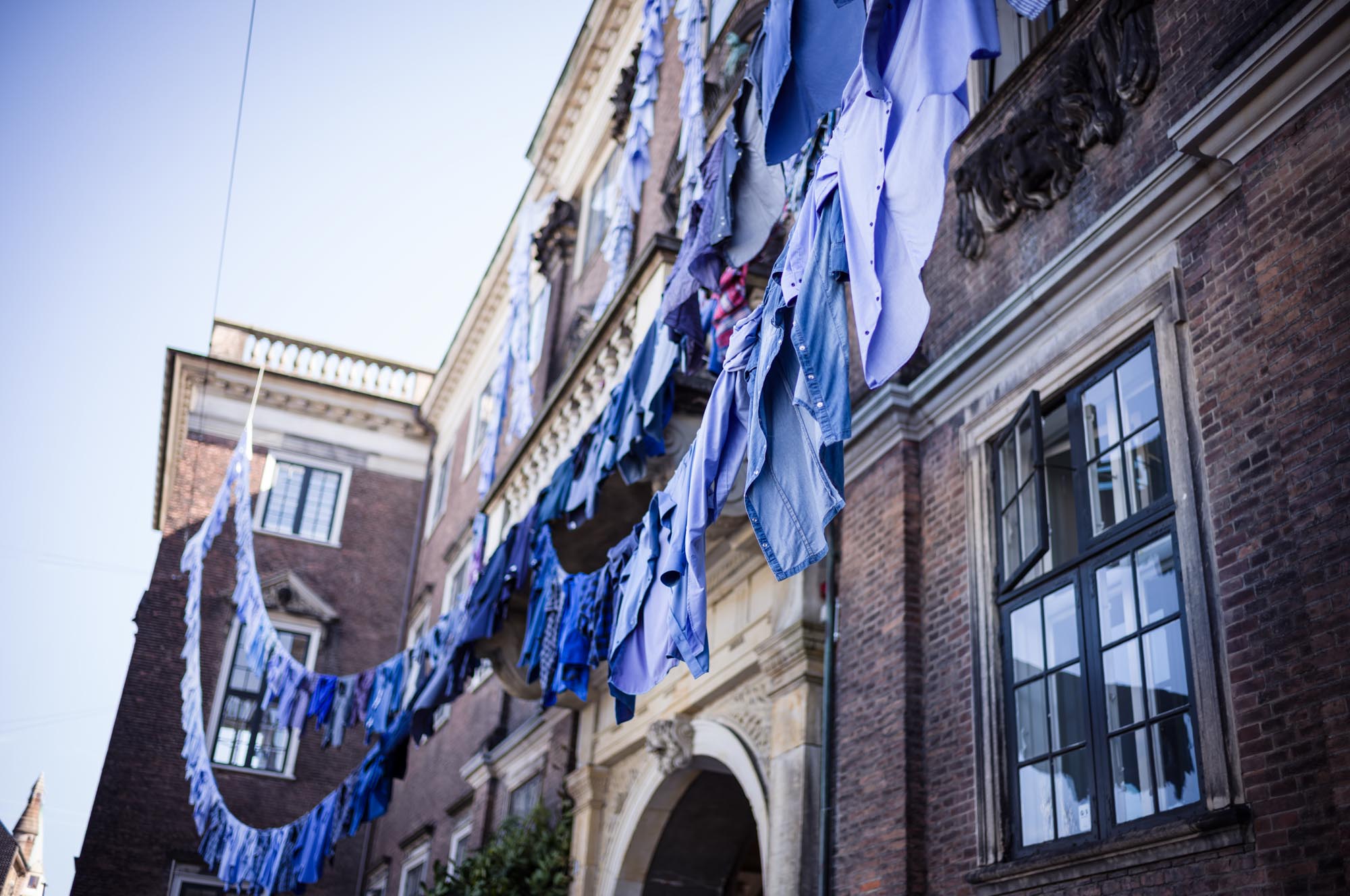 Blue clothes hanging on lines between historic brick buildings under a clear sky.