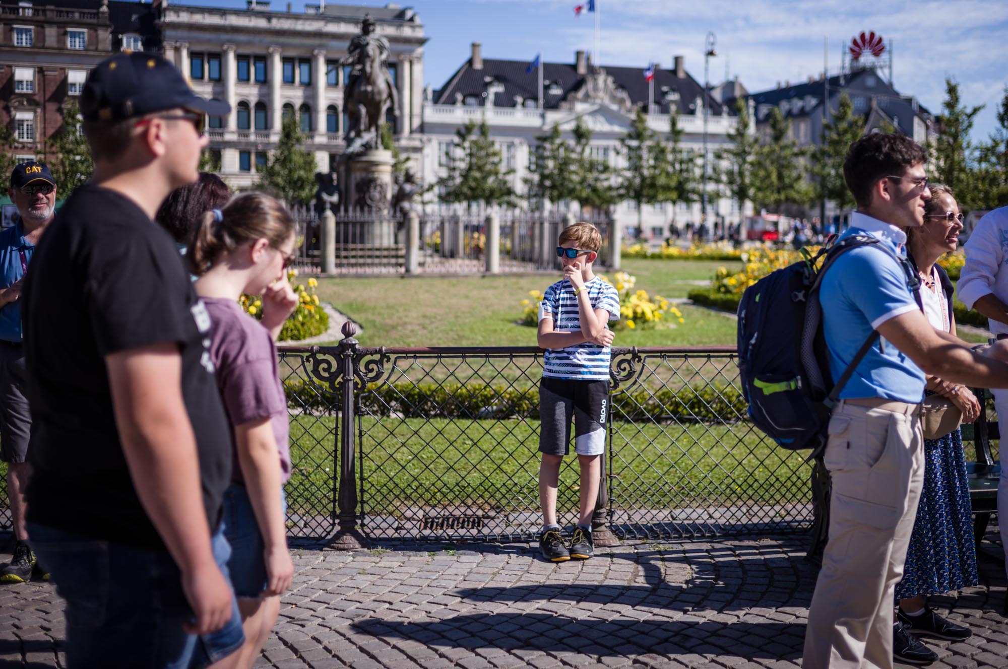 People standing near a historic statue on a sunny day in a city park.