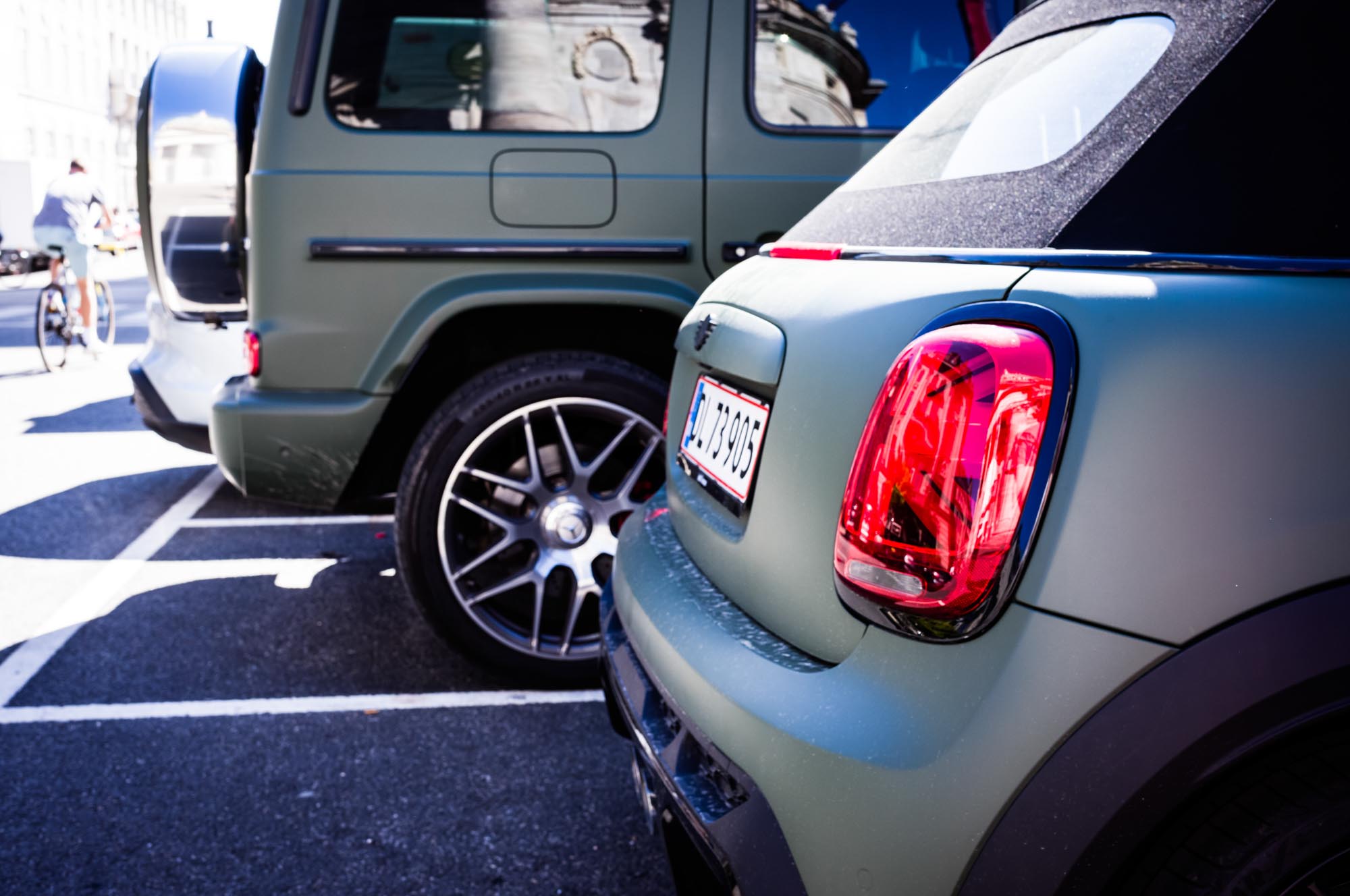Matte green Mini Cooper and SUV parked close together in a bright urban setting.