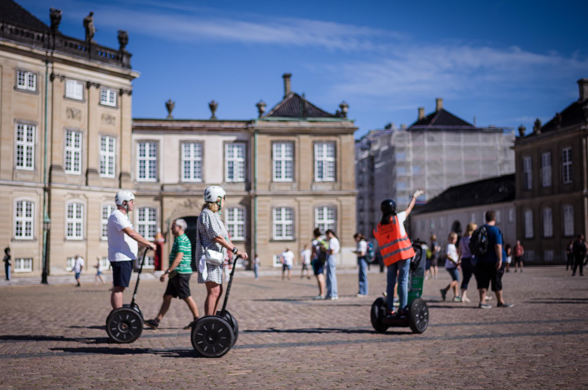 People on Segways touring a historic square with ornate buildings under a clear blue sky.
