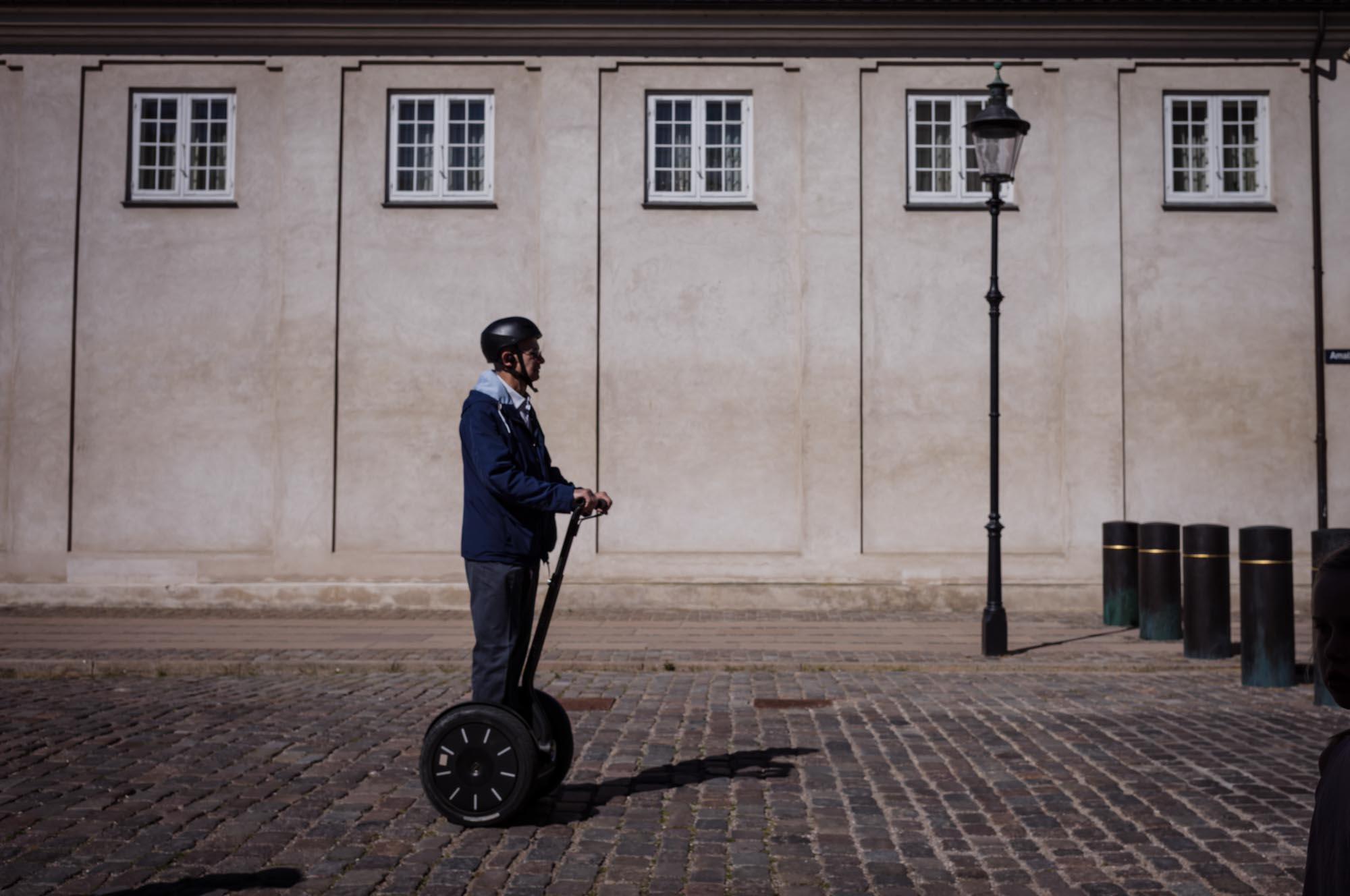 Man riding a Segway on cobblestone street beside a beige building and lamppost.
