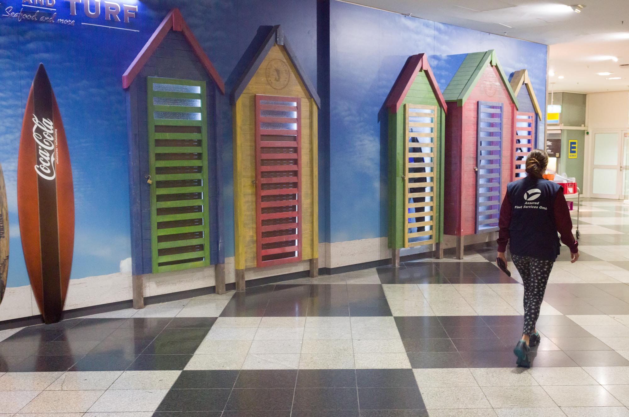Colorful beach hut doors and surfboard wall decor with person walking in a modern hallway.