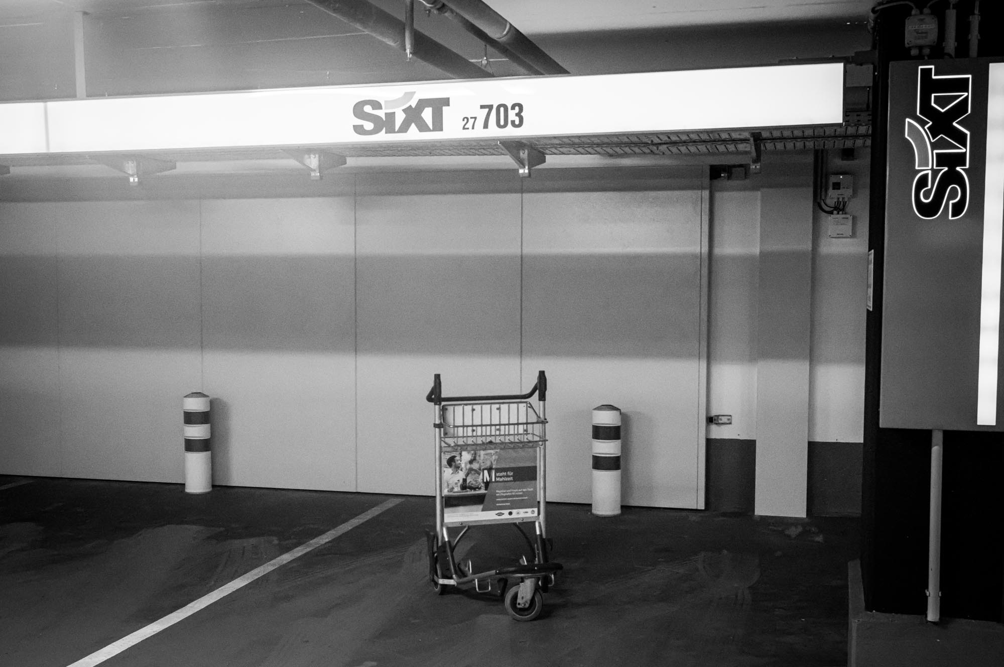 Luggage cart in empty parking space at Sixt rental area, black and white photo.