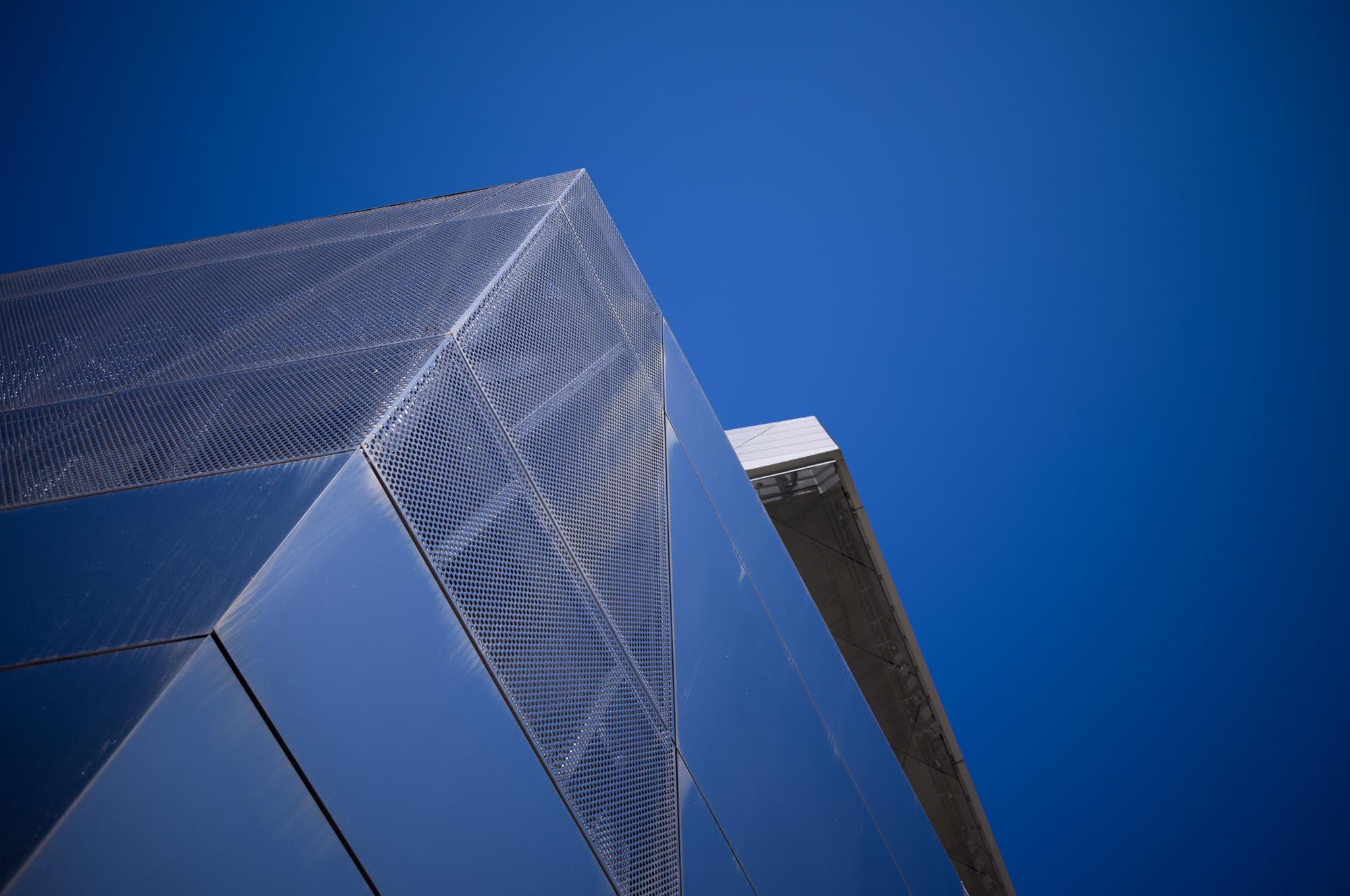 Modern building facade with perforated metal panels against a clear blue sky.