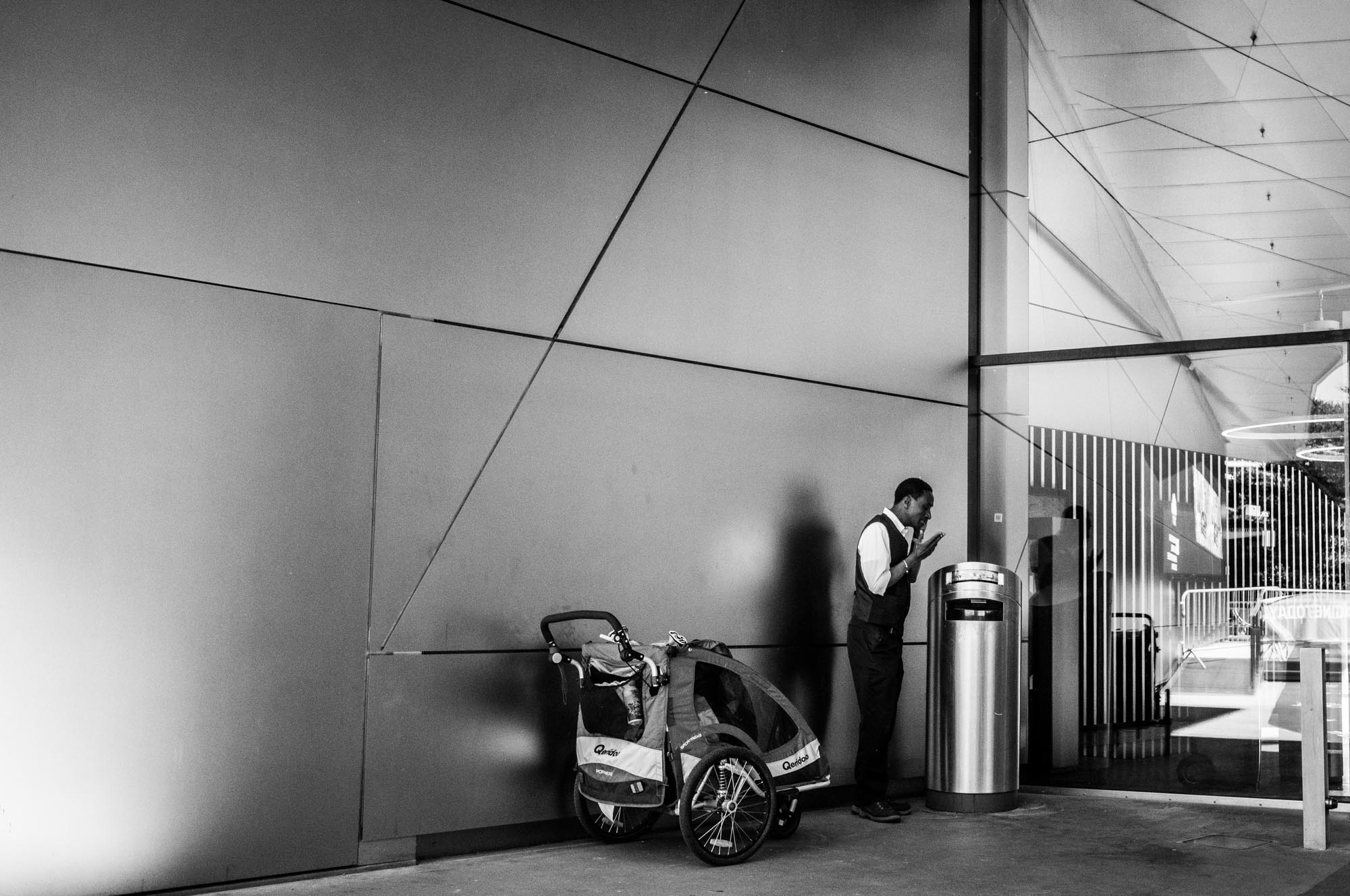 Man using phone beside bike cart in modern building lobby, black and white photo.