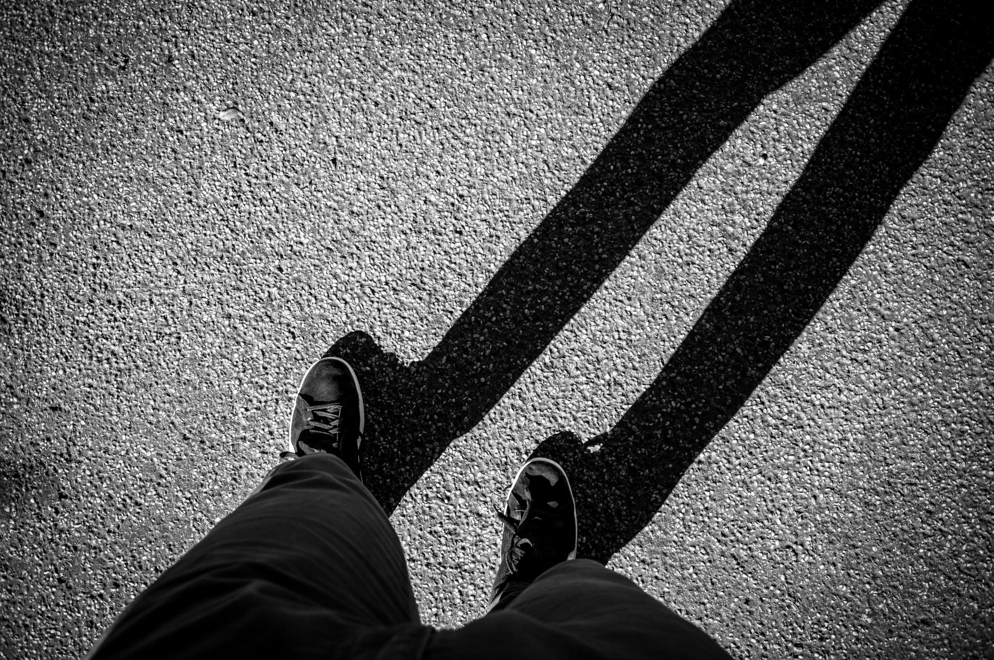 Black and white image of a person’s feet on pavement with a long shadow.