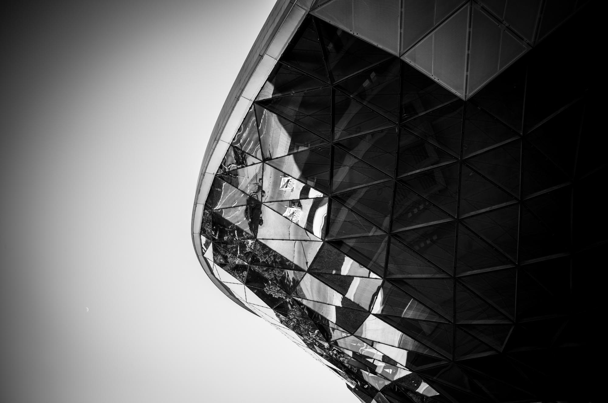 Abstract architecture with reflective, geometric glass facade in black and white against a clear sky.