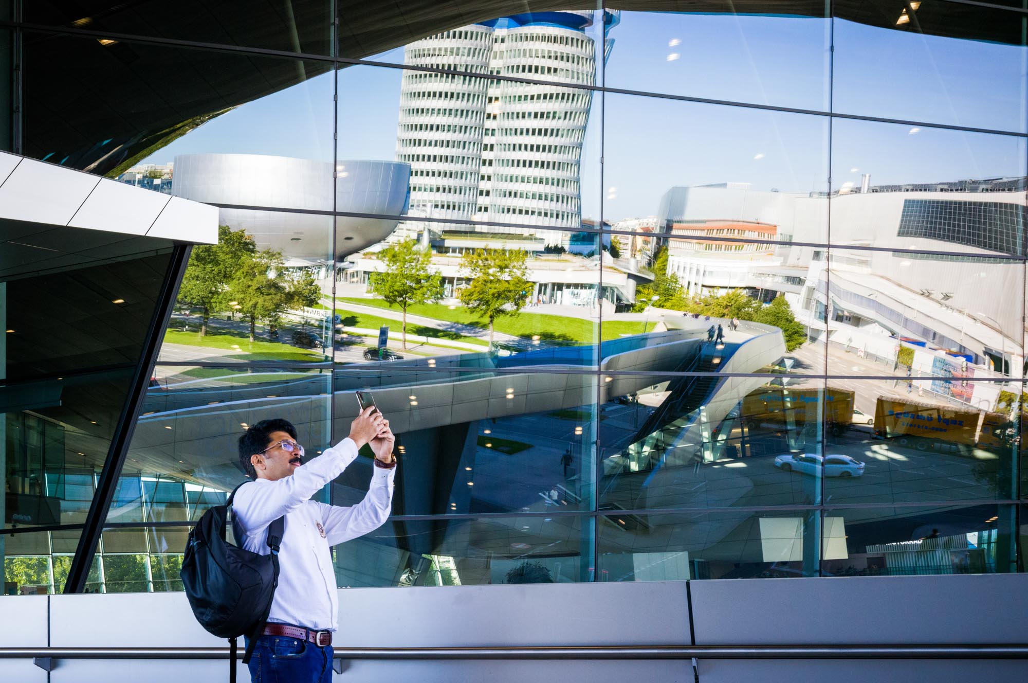 Man taking a photo of modern architecture through reflective glass in urban setting.