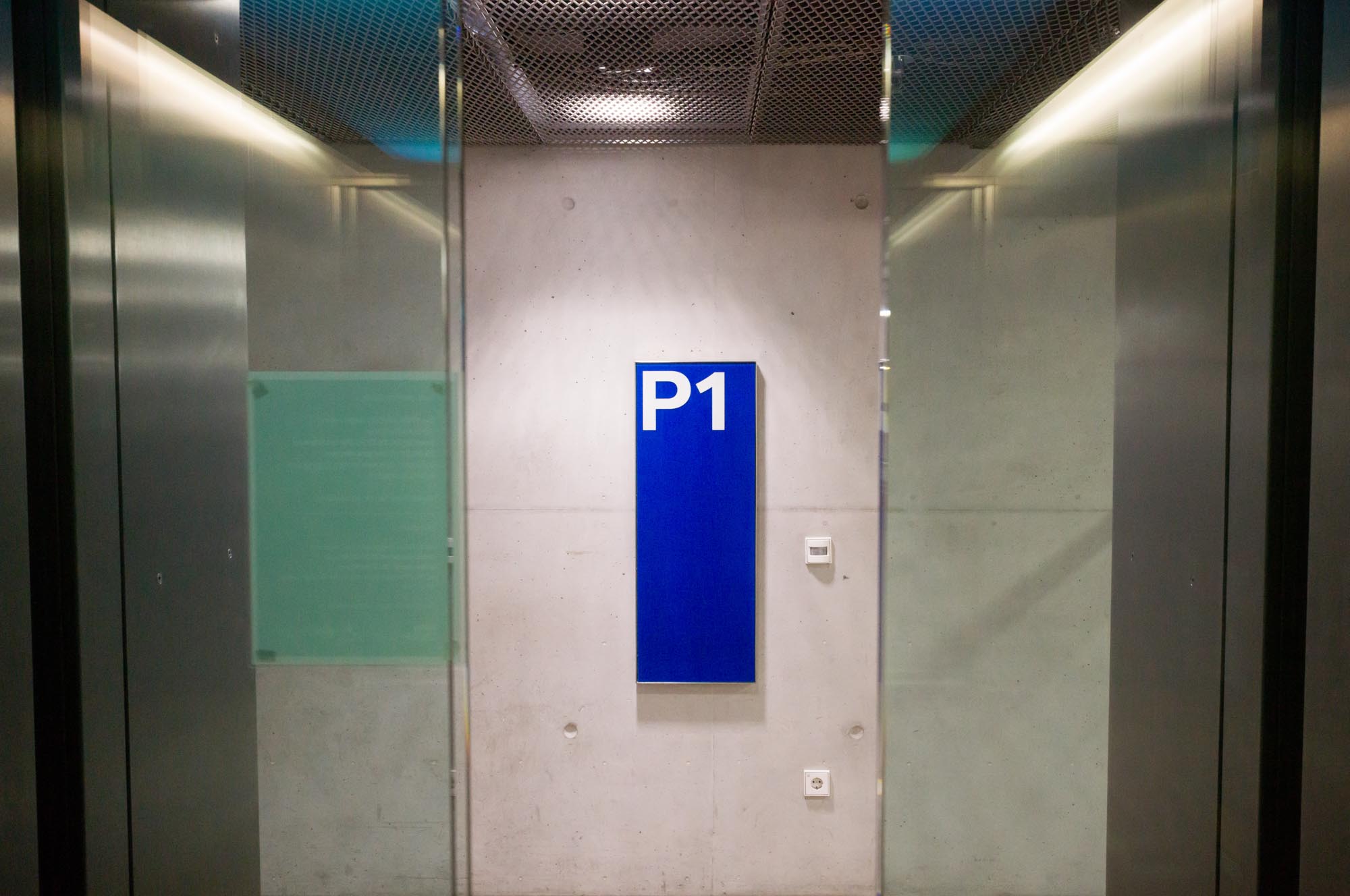 Blue P1 sign on a concrete wall, seen from an elevator perspective.