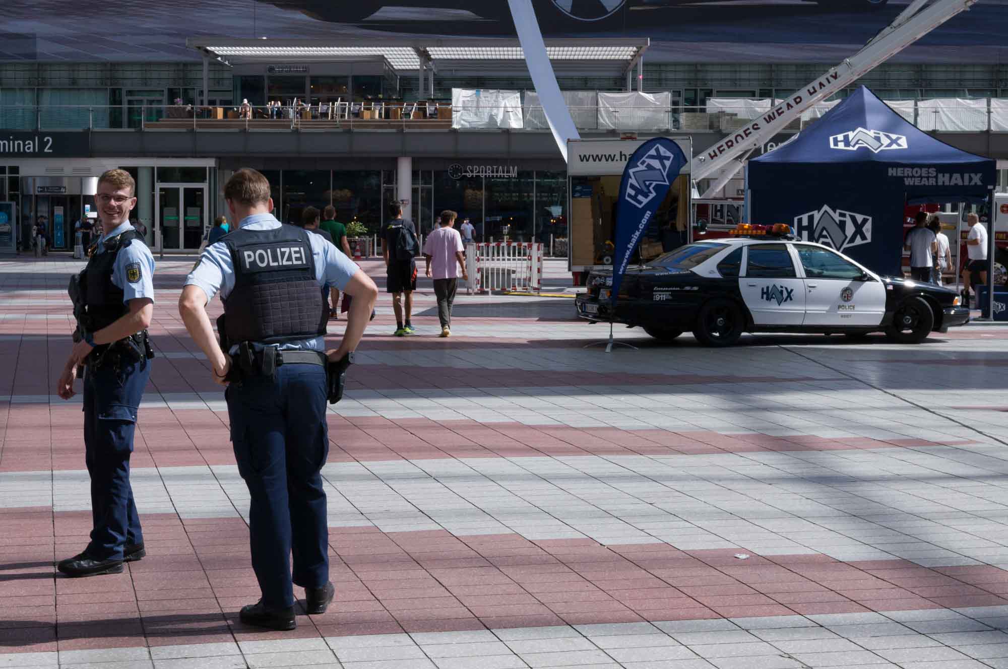 Police officers in uniform stand outside Terminal 2, near a parked police car, during a public event.