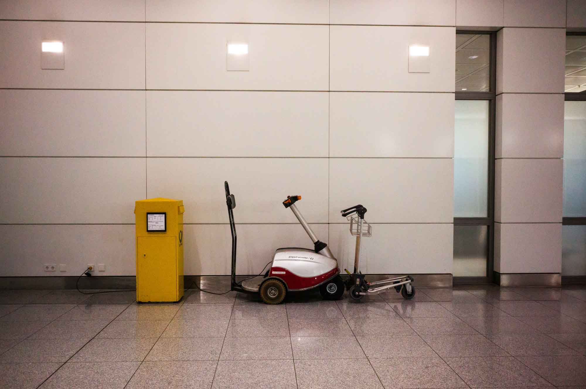 Yellow charging station and airport cleaning equipment against white tiled wall.