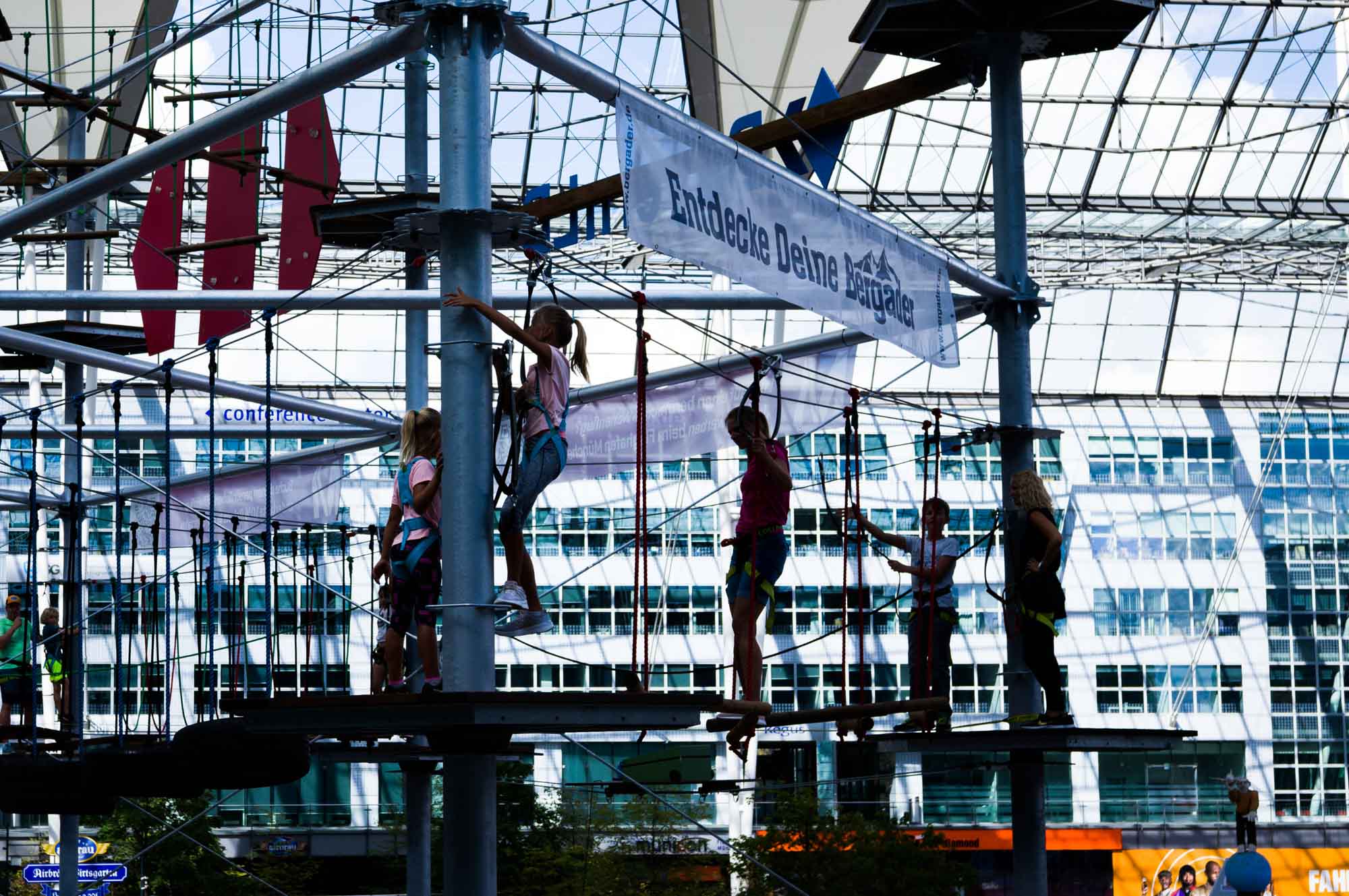 Children enjoying a high ropes course adventure indoors, with harnesses and safety gear.