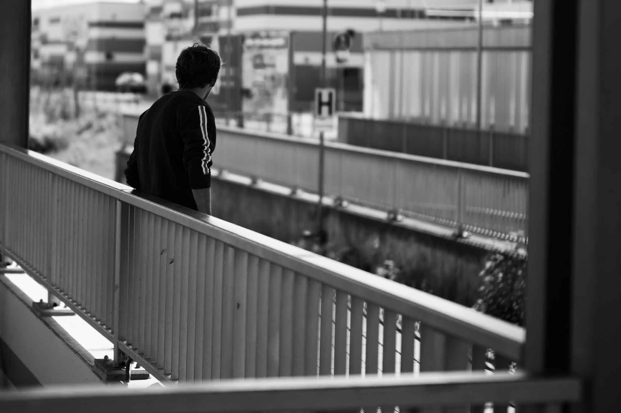 Person walking alone on an urban bridge, captured in black and white, conveying solitude and city life.