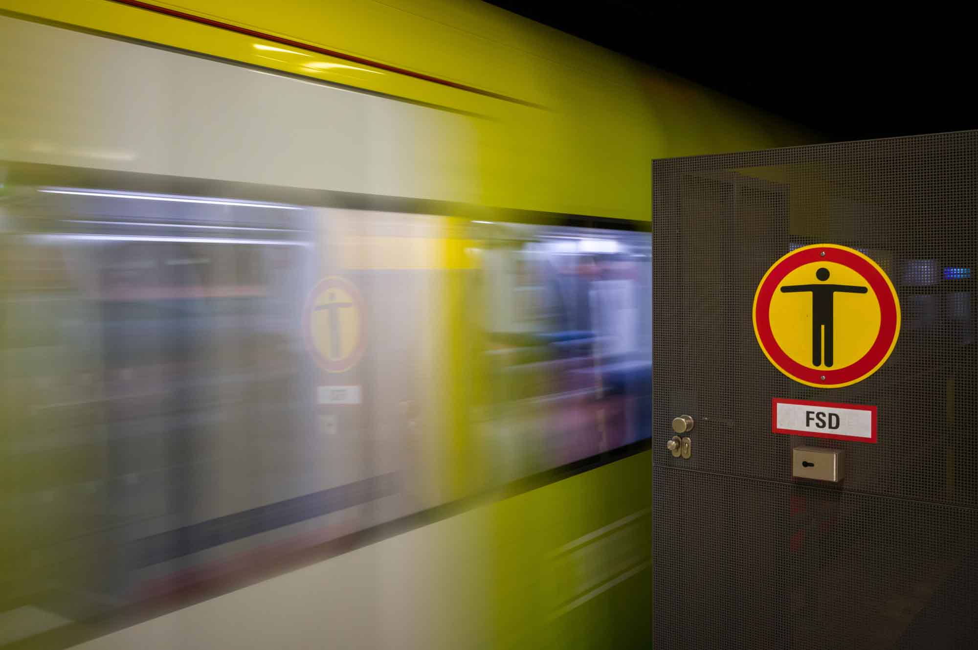 Blurred yellow train passing Do Not Enter sign at a metro station.