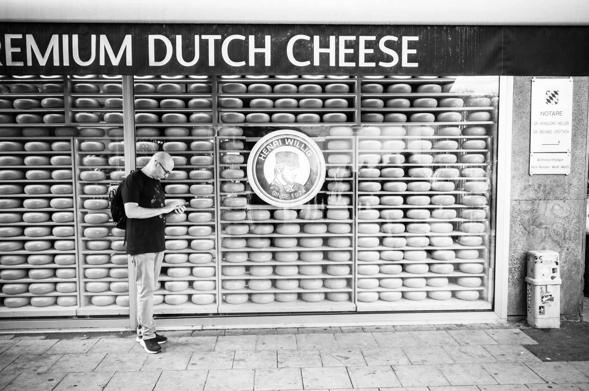 Person standing by a shop window filled with wheels of Dutch cheese in black and white.
