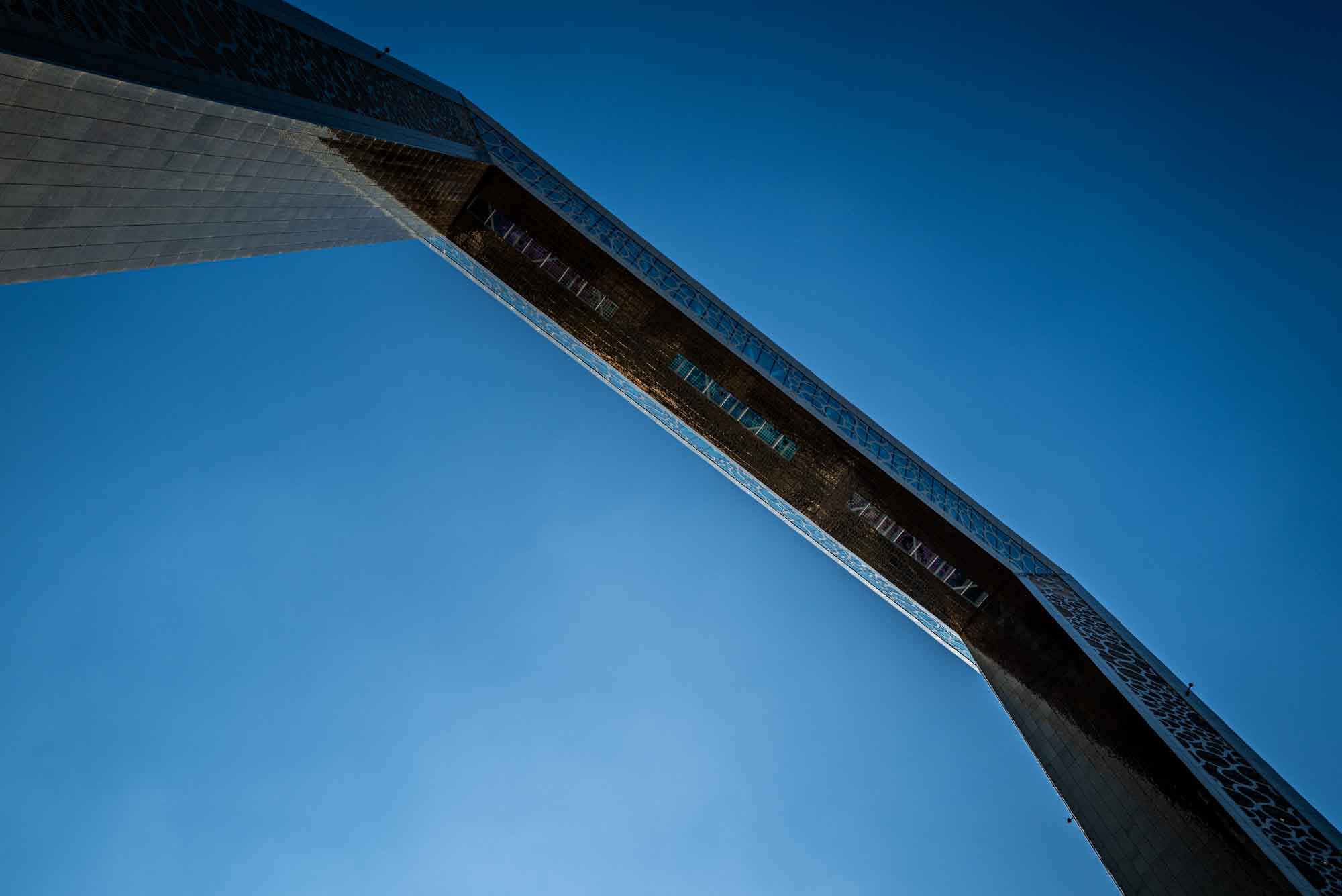 Futuristic architectural structure against clear blue sky, viewed from below. Modern design and engineering marvel.