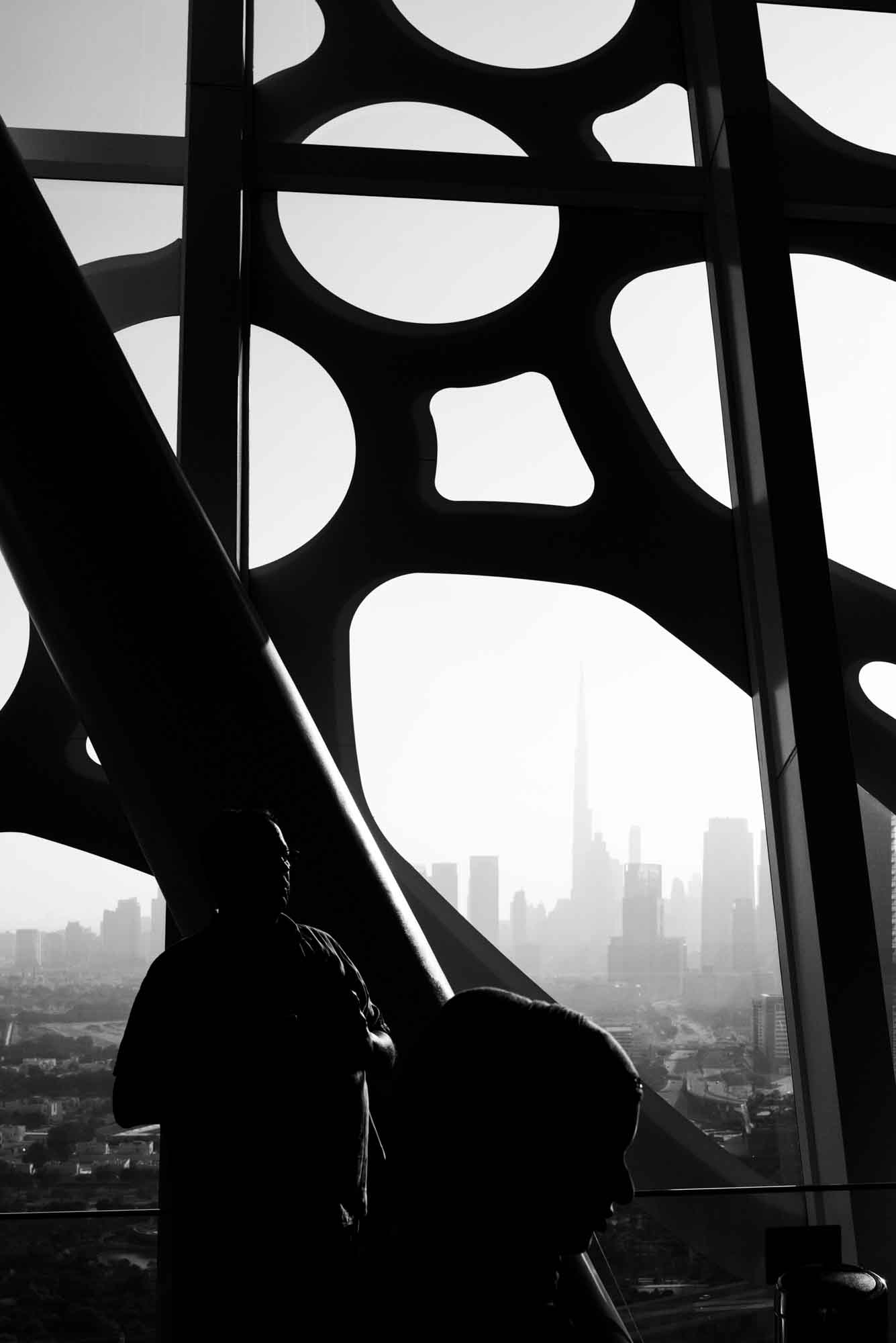 Silhouette of people inside modern building with city skyline and iconic tower in the background.