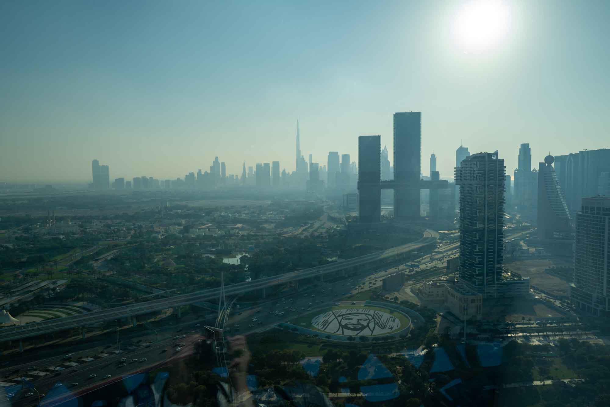 Skyline of Dubai with Burj Khalifa in the distance under a bright sun, showcasing modern architecture and urban landscape.