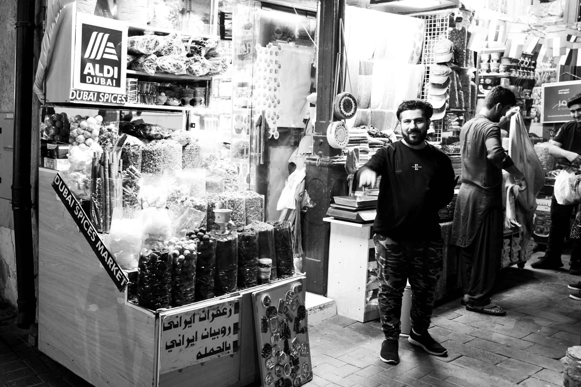 Man in spice market with diverse products, Dubai Spices Market in black and white ambiance.