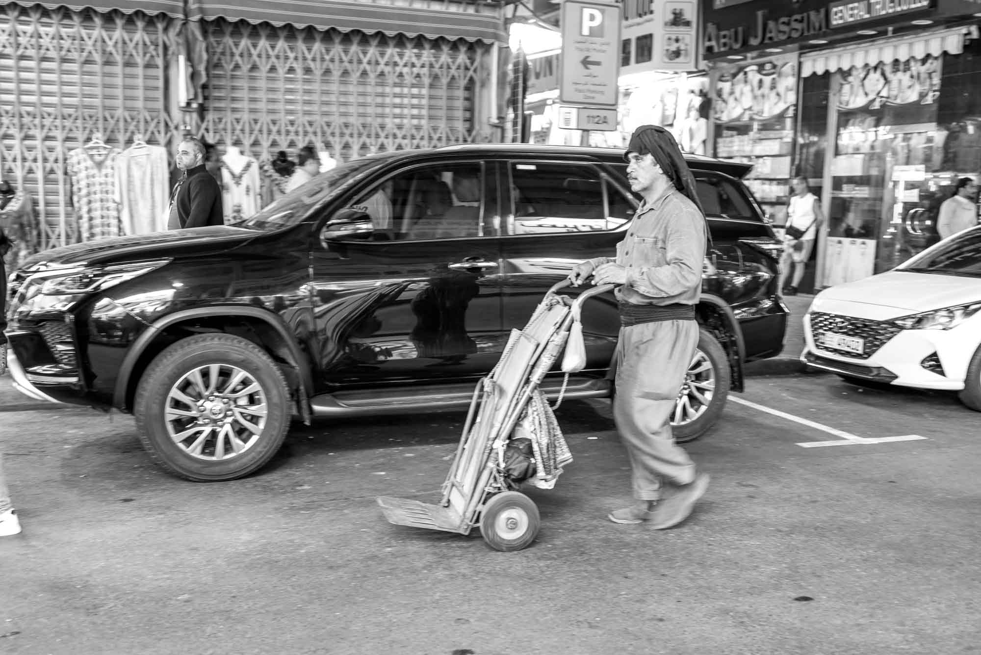 Man pushing a handcart in a busy market street, black and white photo.