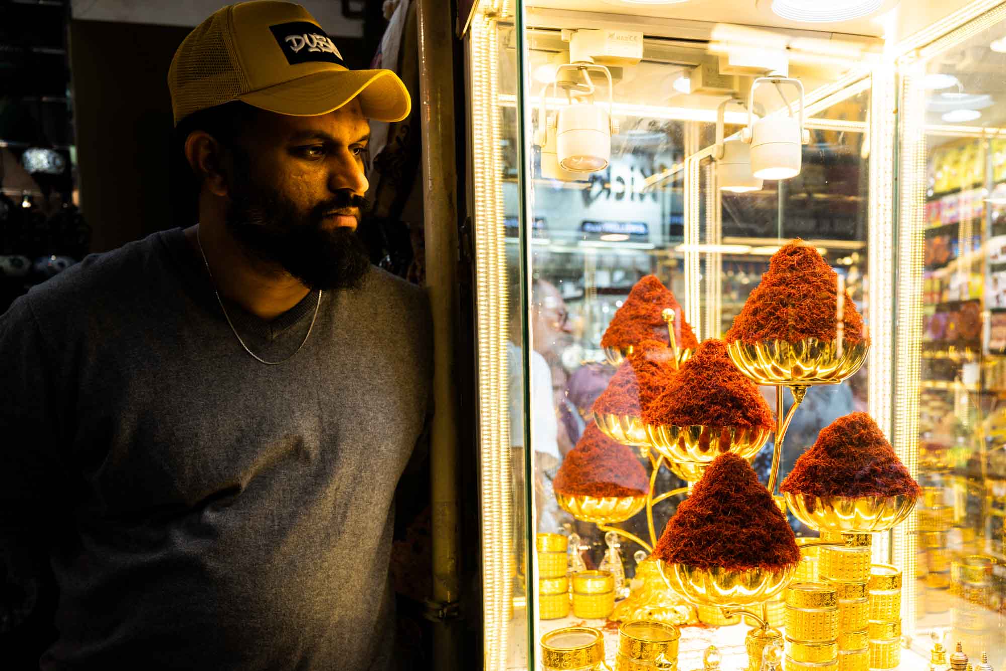 Man admiring vibrant saffron display in Dubai spice market under warm light.