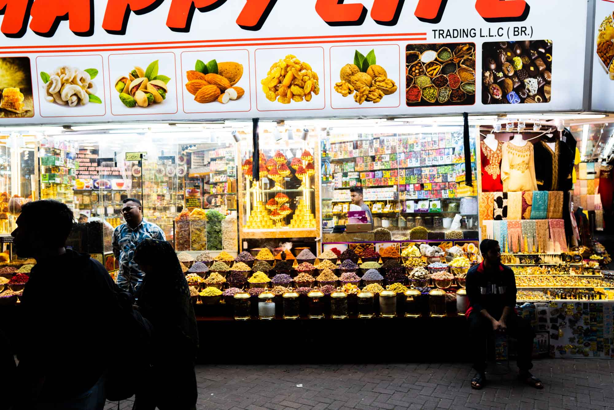 Bustling spice and textile market shop at night with colorful displays and busy atmosphere.