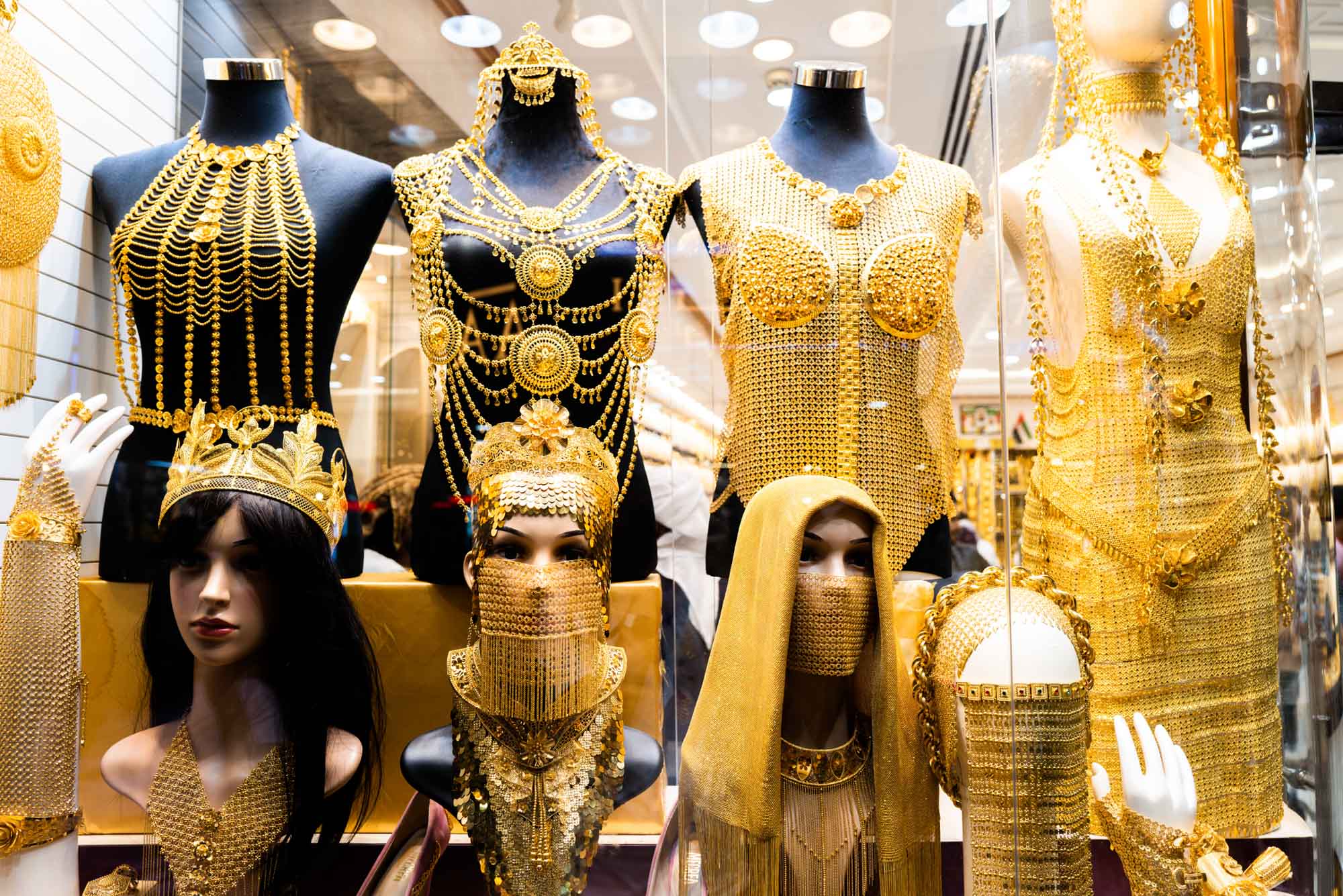 Luxurious gold jewelry display with elaborate necklaces, crowns, and veils on mannequins in a store.