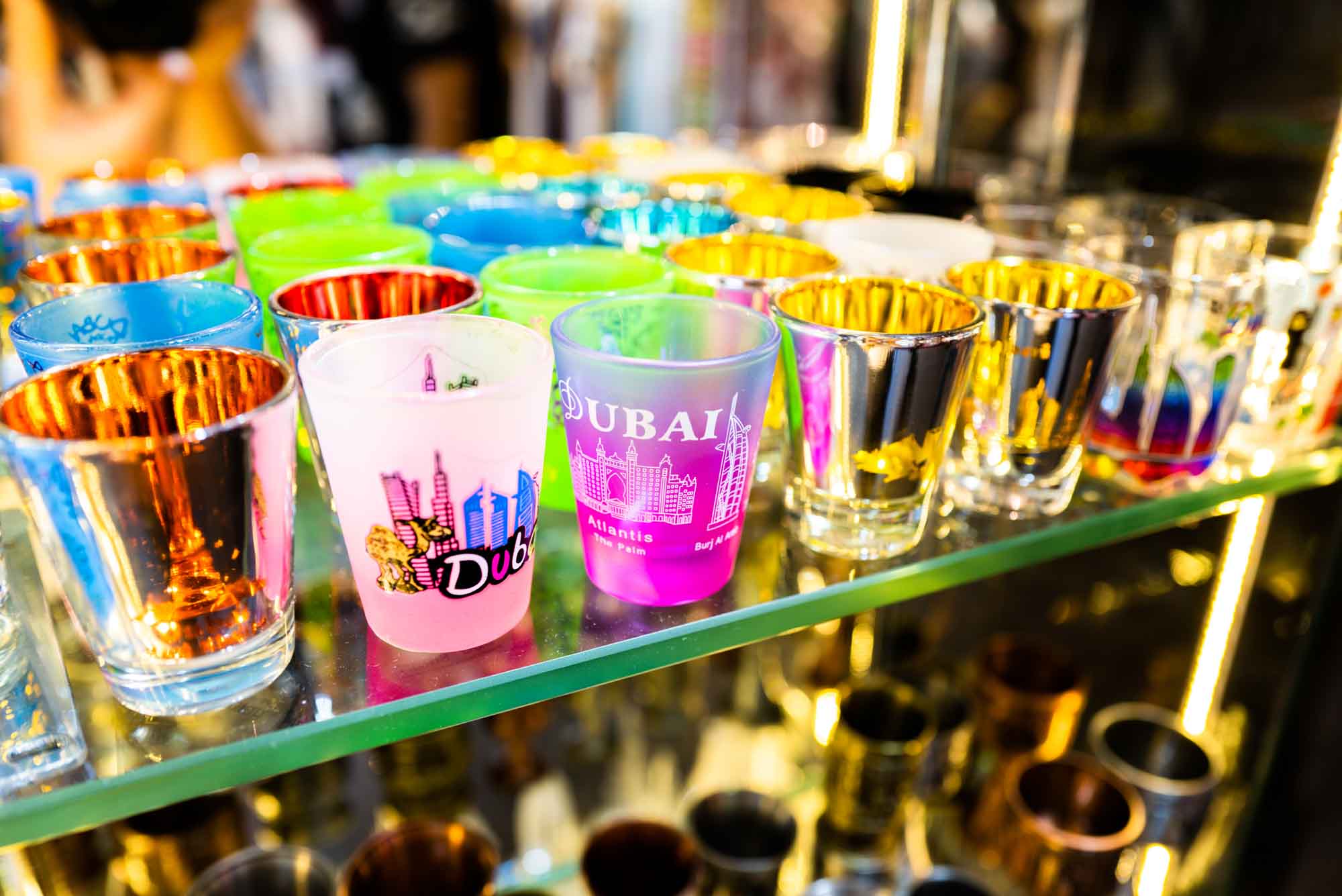 Colorful Dubai souvenir shot glasses on display shelf.