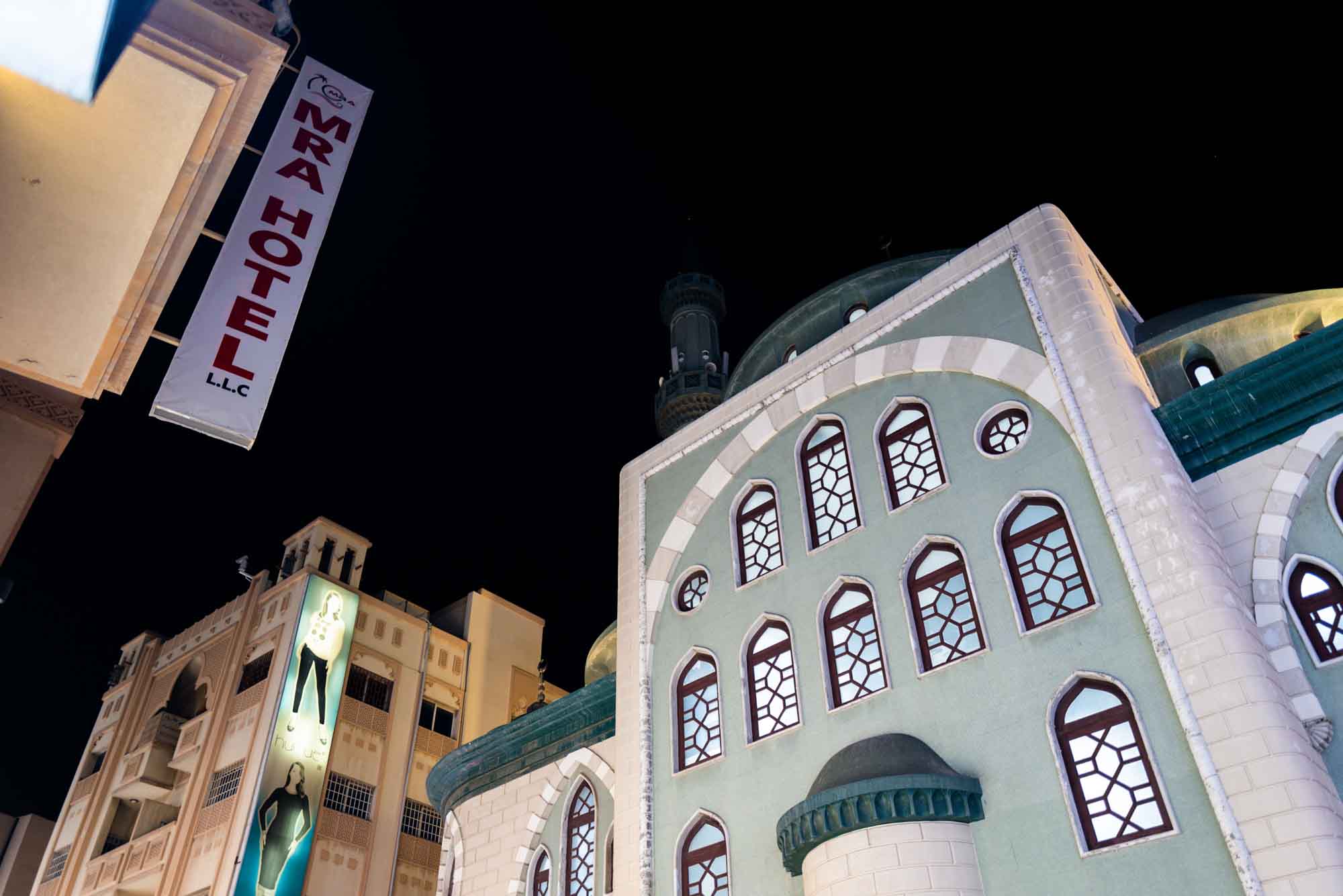 Night view of buildings with MRA Hotel sign and architectural details, set against a dark sky.