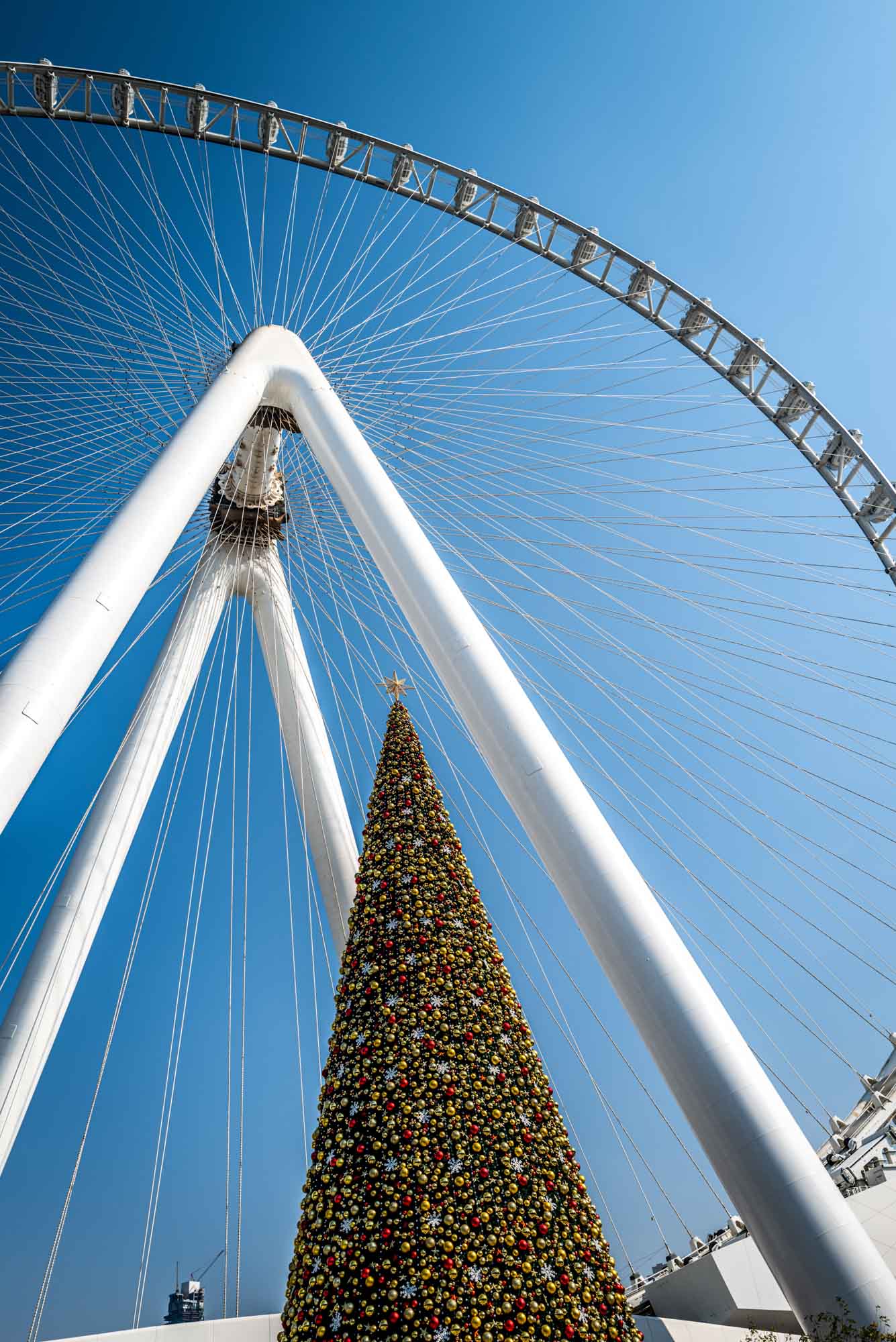 Ferris wheel with festive Christmas tree against a clear blue sky.