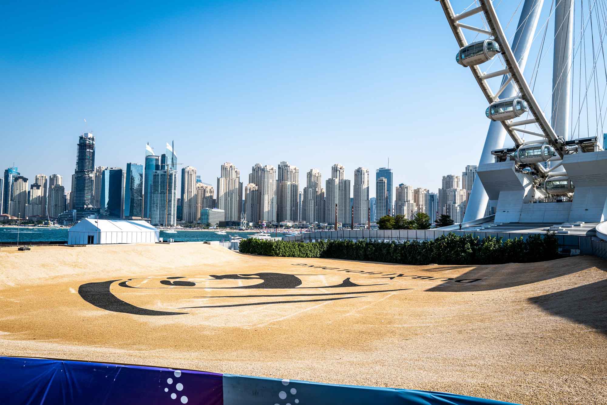 Skyline view of Dubai with modern skyscrapers and a large Ferris wheel by the waterfront, under a clear blue sky.