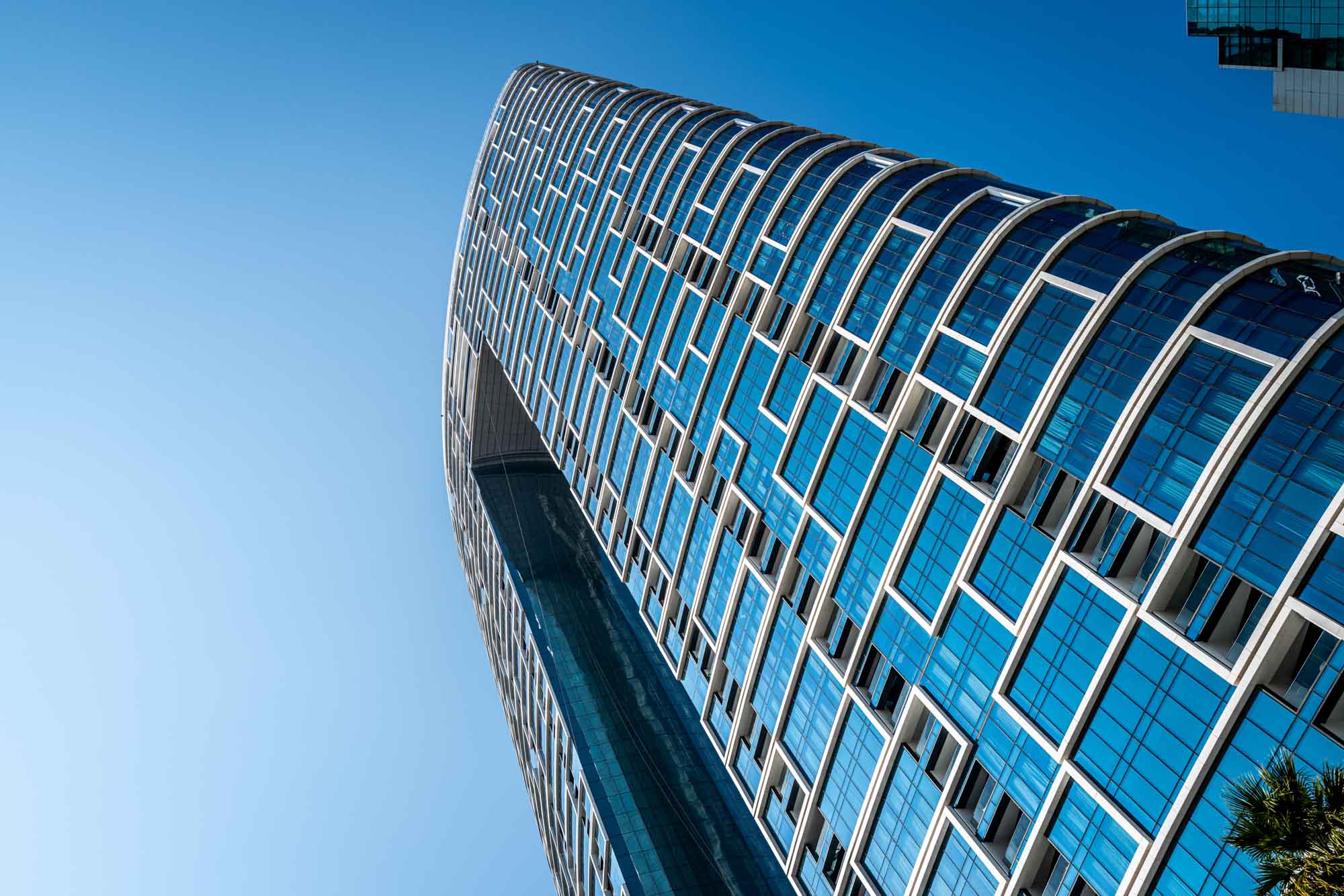 Futuristic skyscraper with glass facade against a clear blue sky, showcasing modern architecture design.