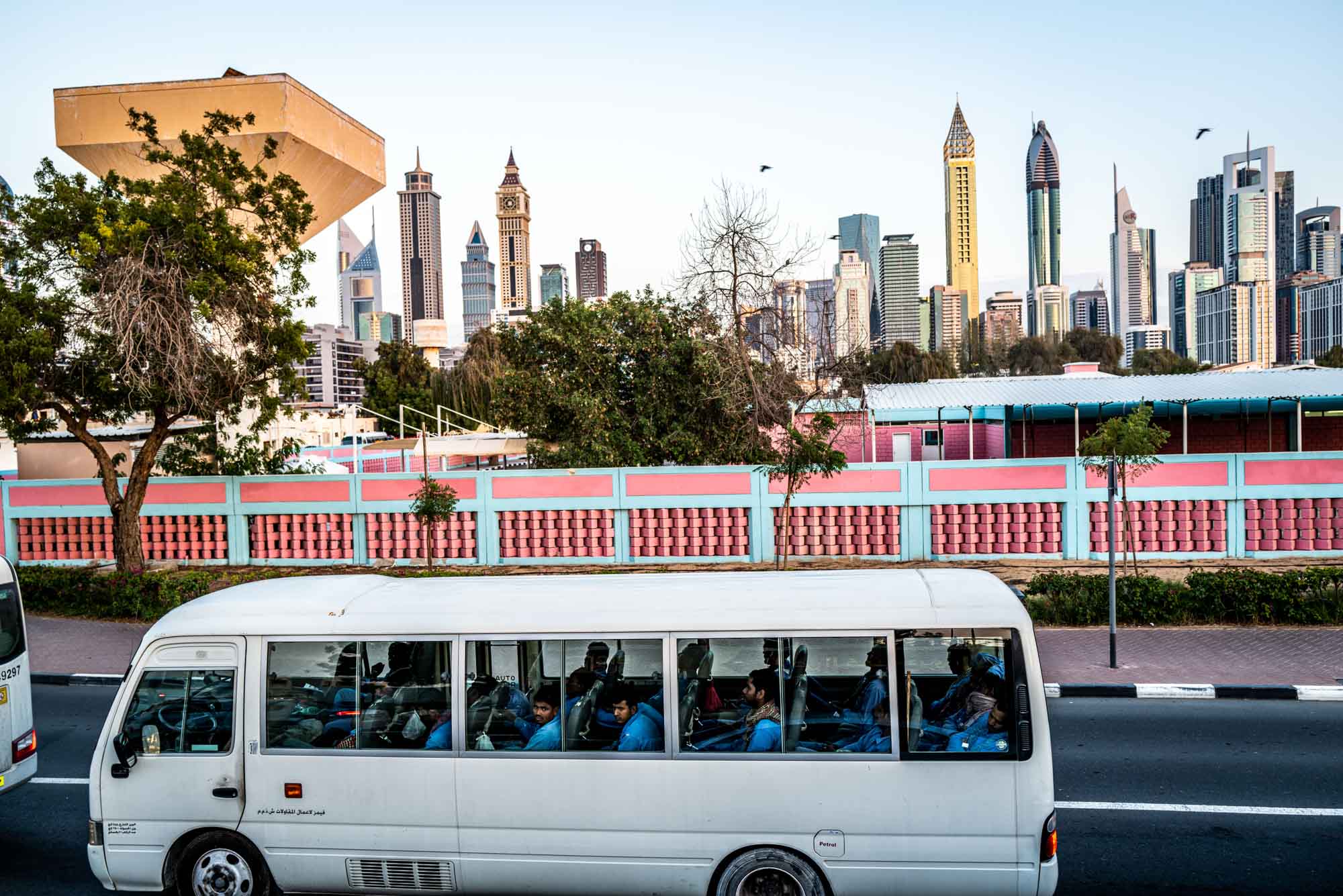 Bus driving past colorful wall with Dubai skyline in the background.