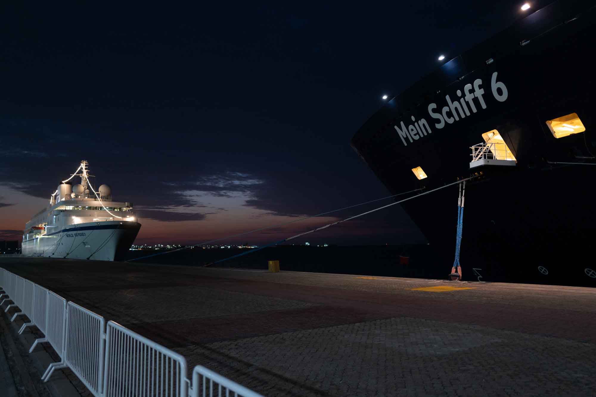 Cruise ships docked at night with illuminated decks, set against a dark sky and a peaceful harbor background.